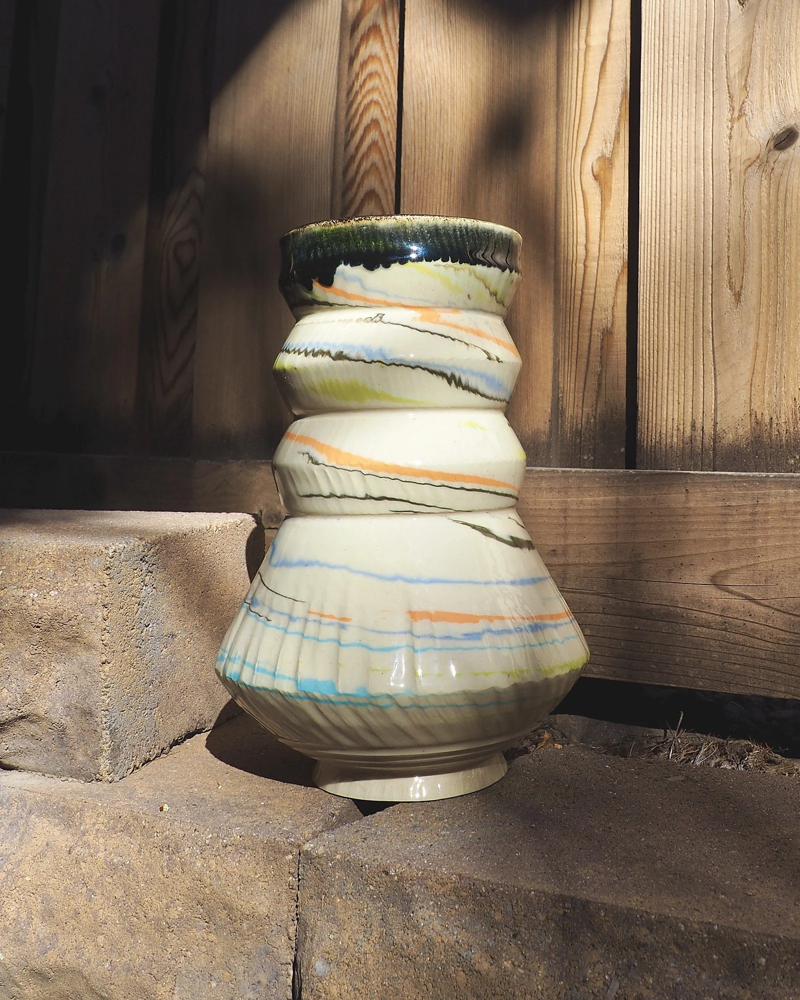 Marbled clay swirl vase in sunlight against a wooden fence