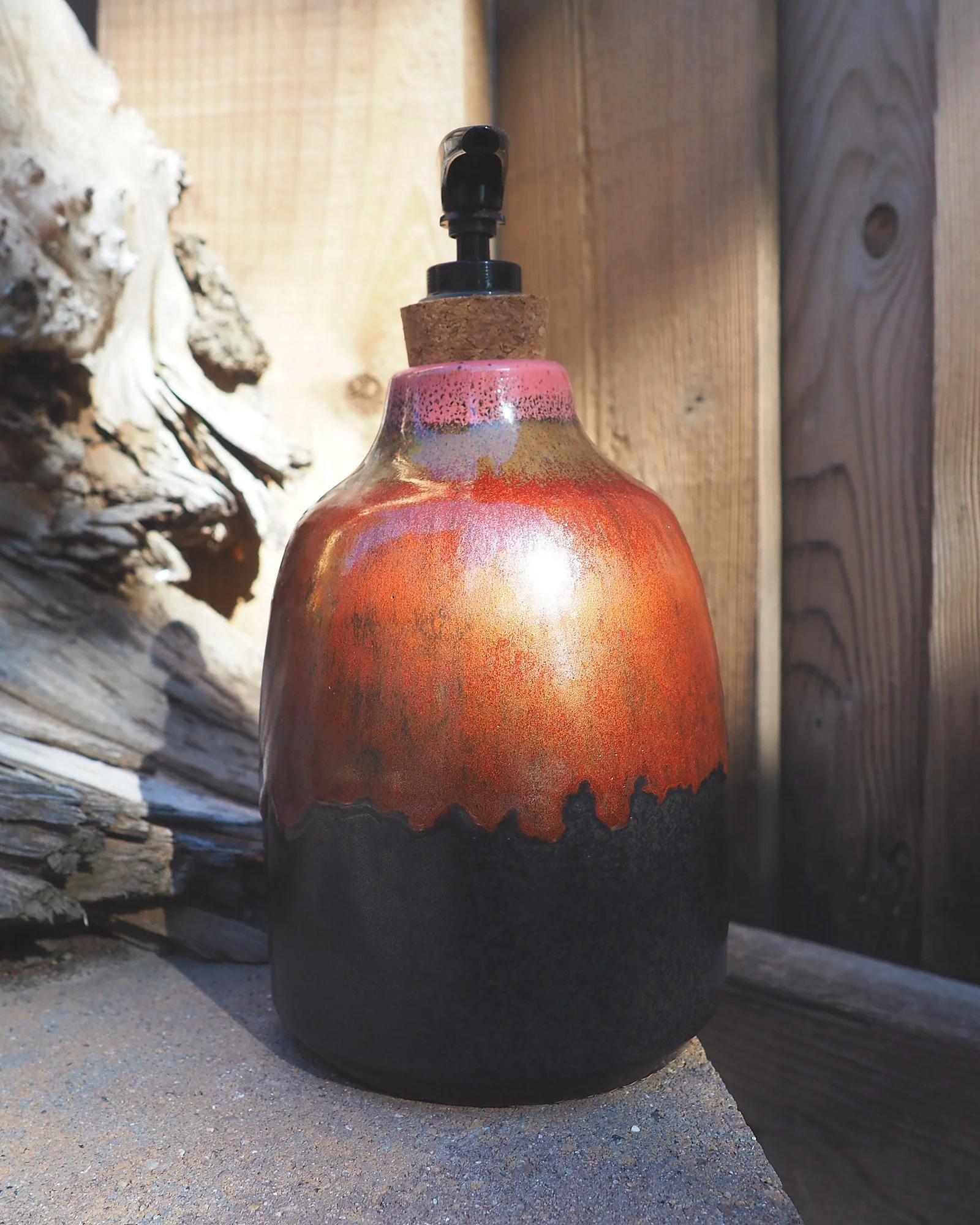 Red drip glaze soap dispenser in sunlight on a stone ledge