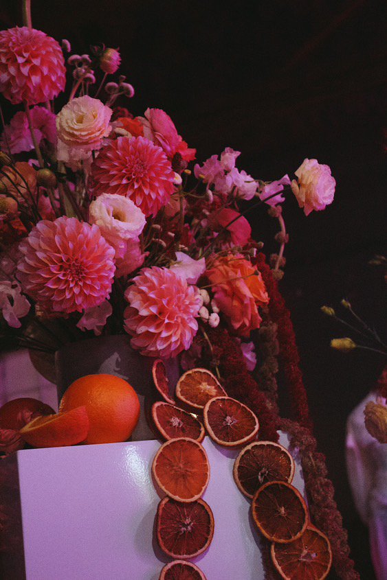 A bouquet of pink and white flowers in a vase, decorated with dried orange slices, on a white surface against a dark background. Marietta Flower Delivery.