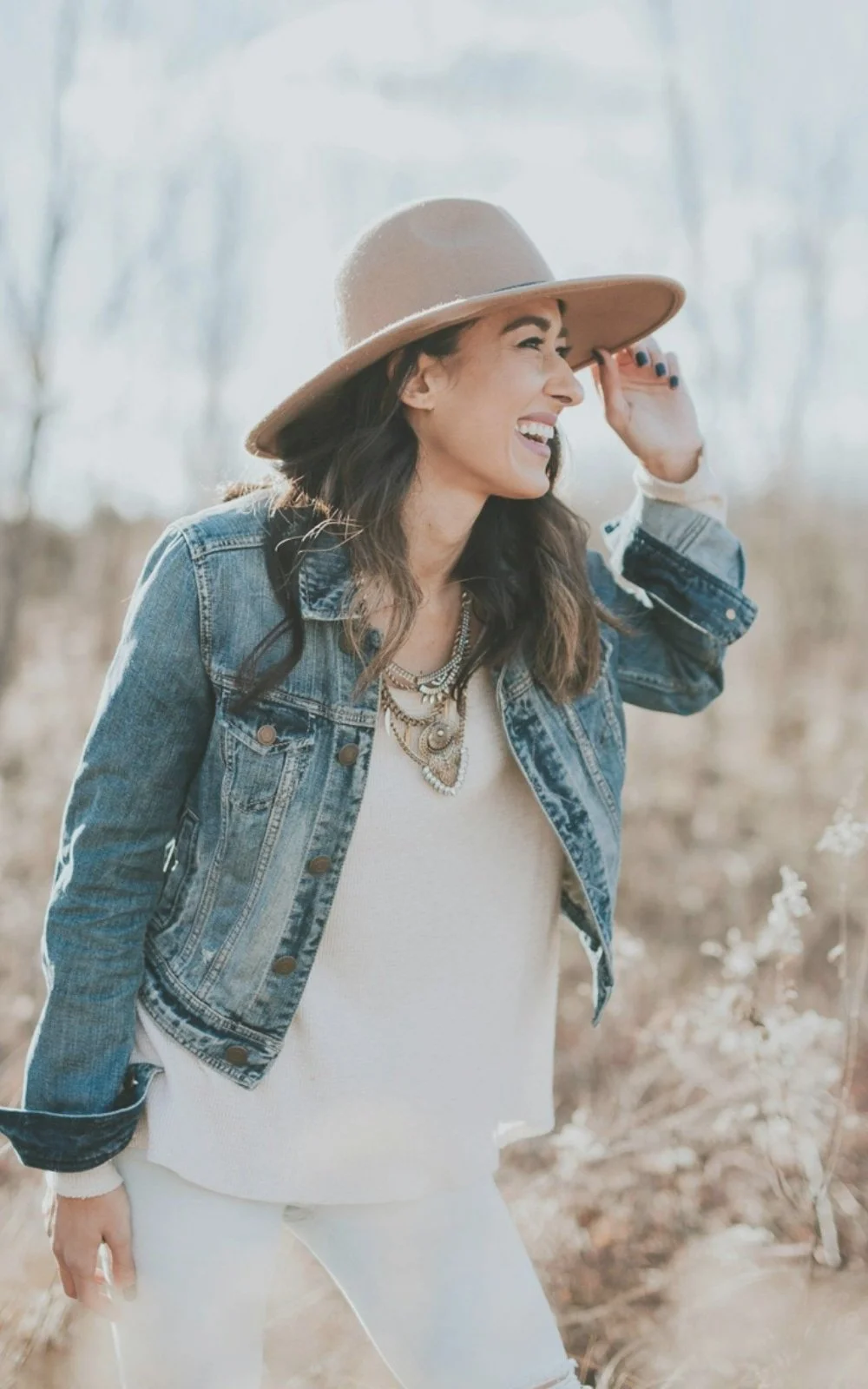A woman standing outside, smiling about her session with therapist Gail Gerbig at Seaside Mental Wellness, wears a hat, jacket, top, and necklace.