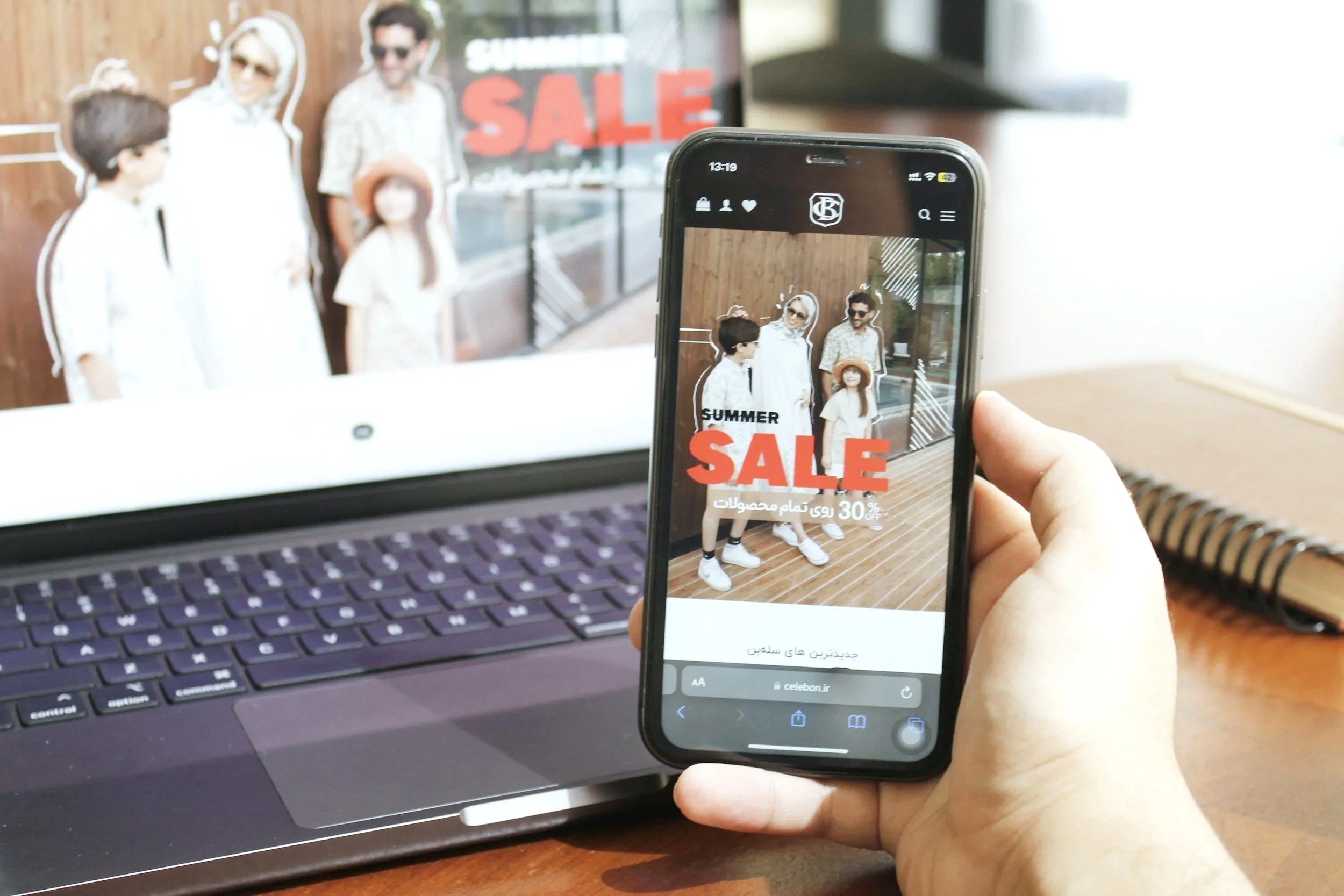 hand holding a mobile phone in front of a laptop