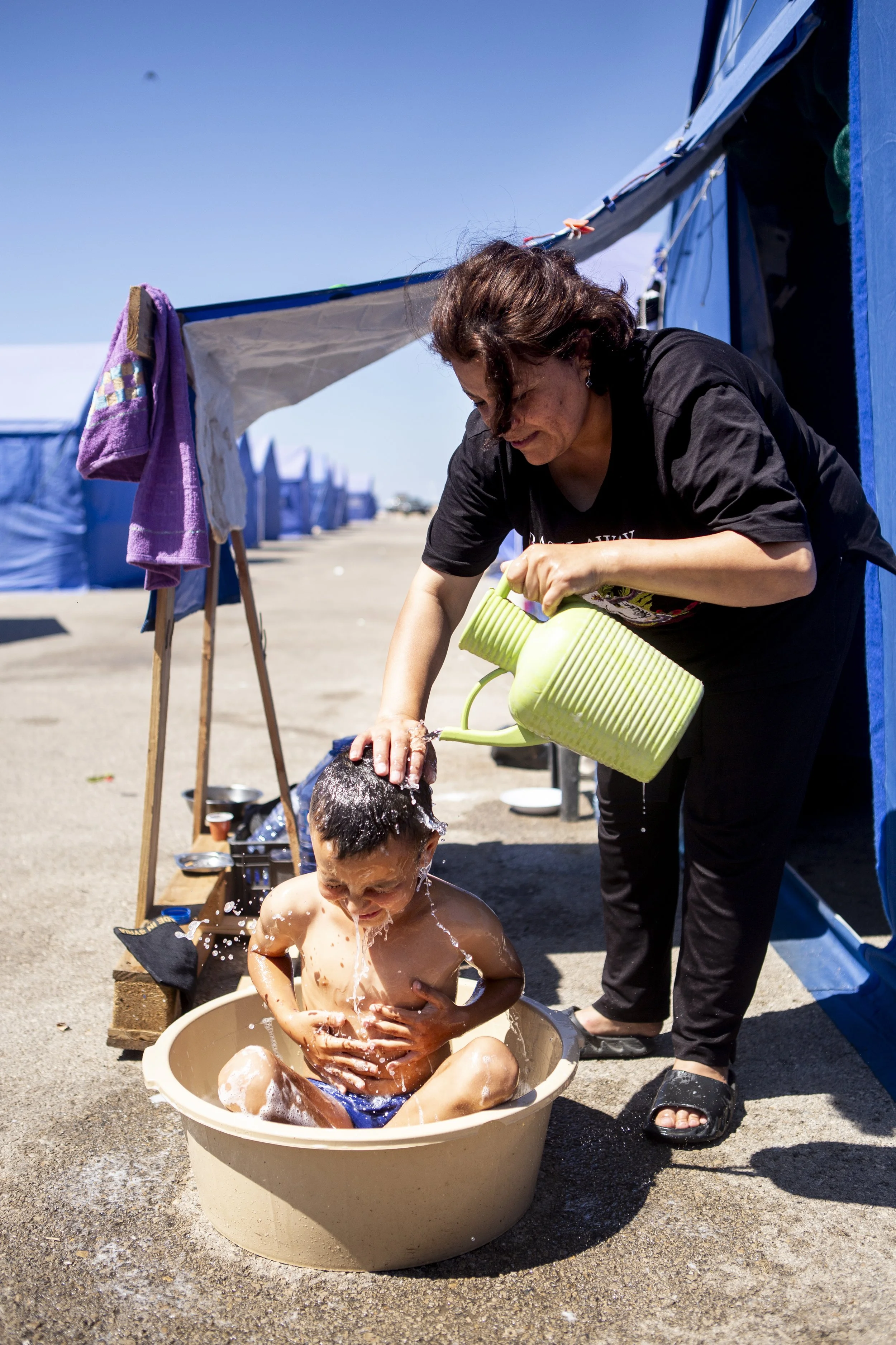 Fatma gives her son, Adam, a bath in a tub with water she has bought. 
