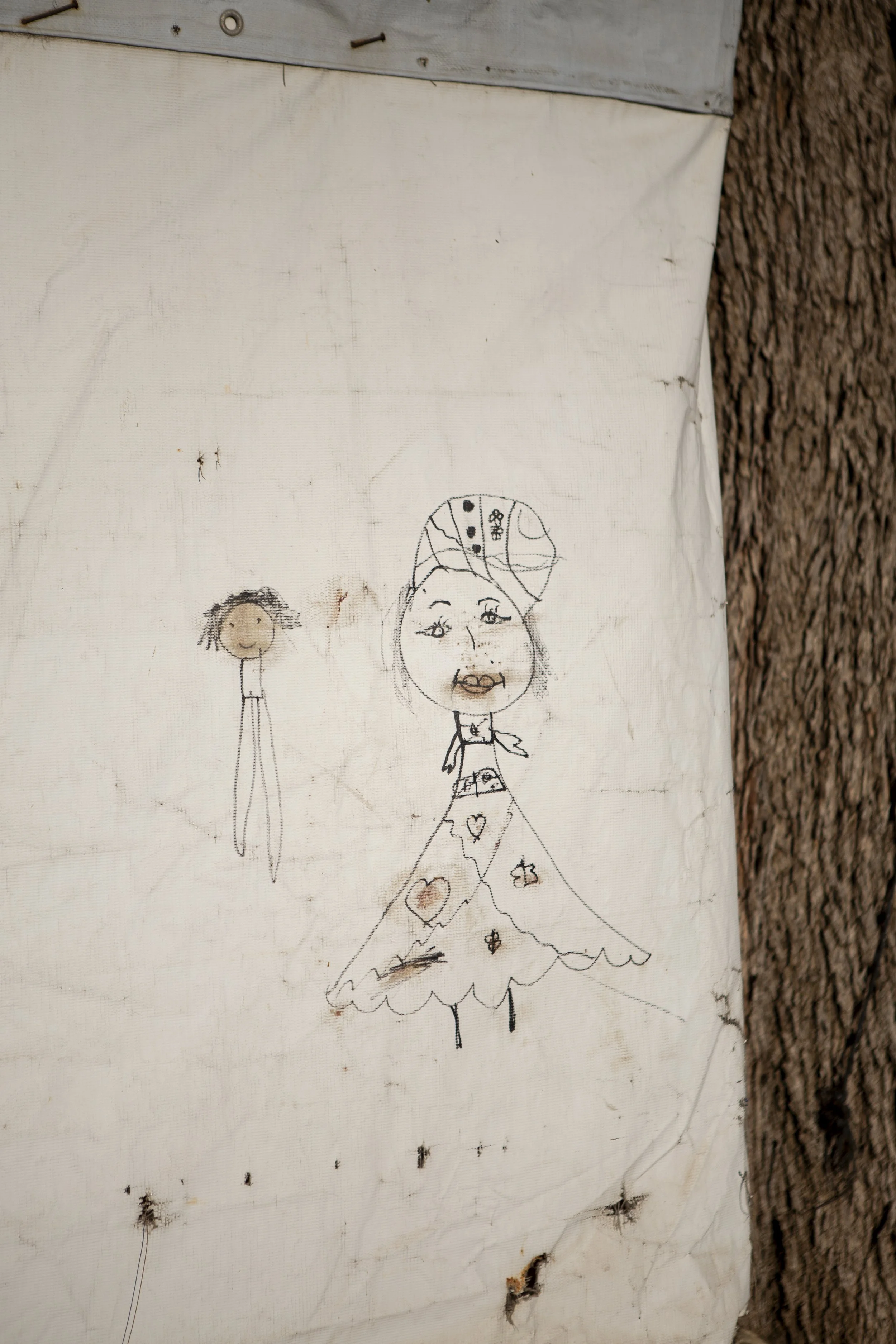 The children of Mariam’s neighbours have drawn figures on their tent. These neighbours are among the few families still remaining. Once a lively informal settlement for Syrian refugees, the area has gradually emptied leaving behind traces.
