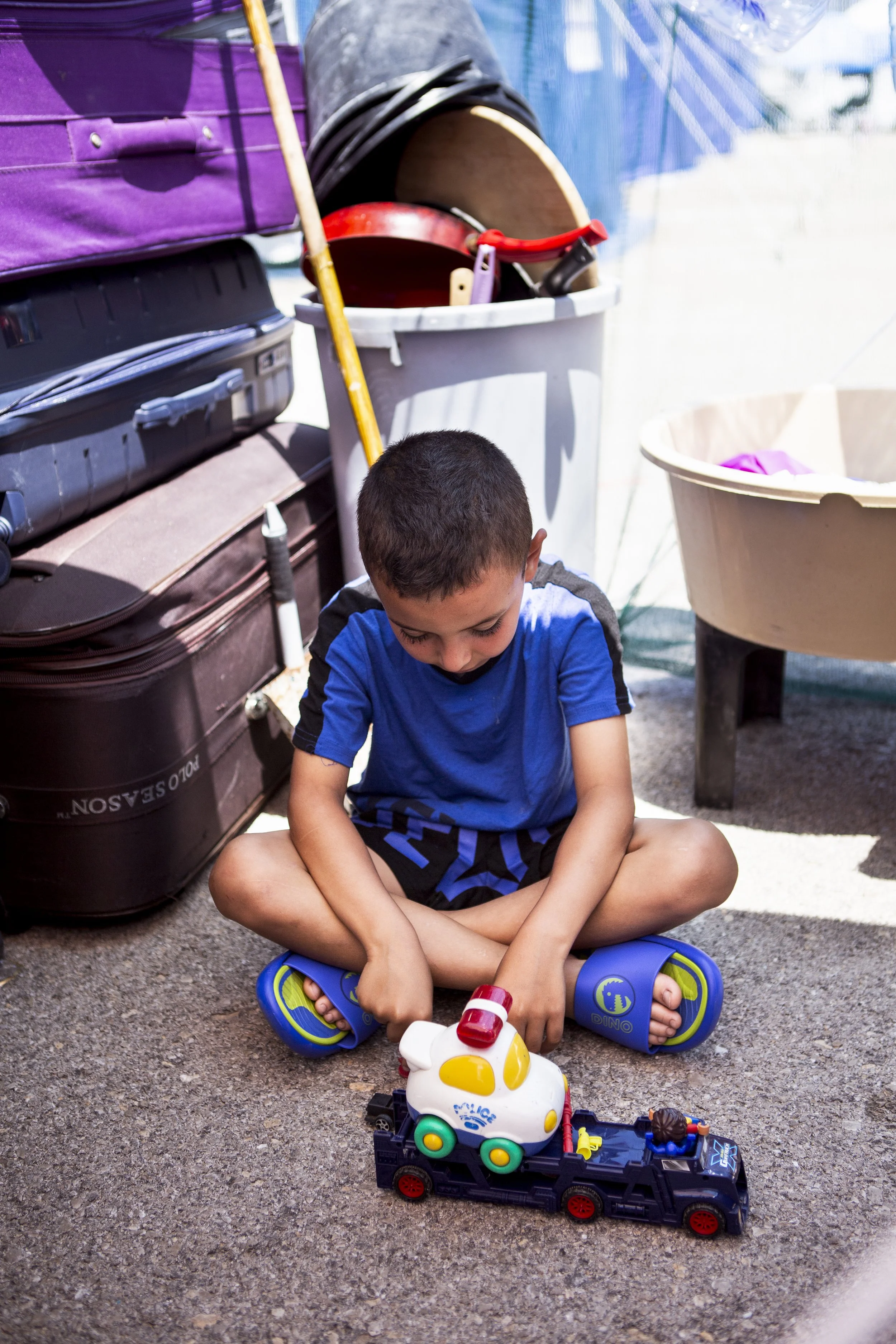 Adam plays on the ground beside his tent under a make shift shelter his family have created to ensure they are protected from the sun.