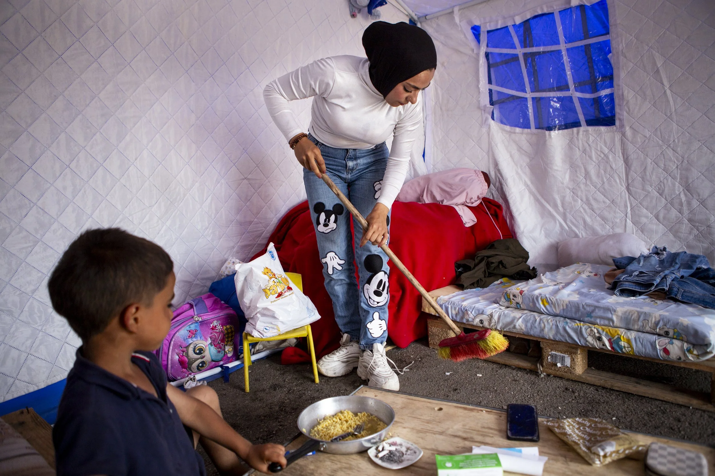 Elisa cleans her tent while her son eats. Originally from Dahiyeh, she is displaced as a single mother. 

