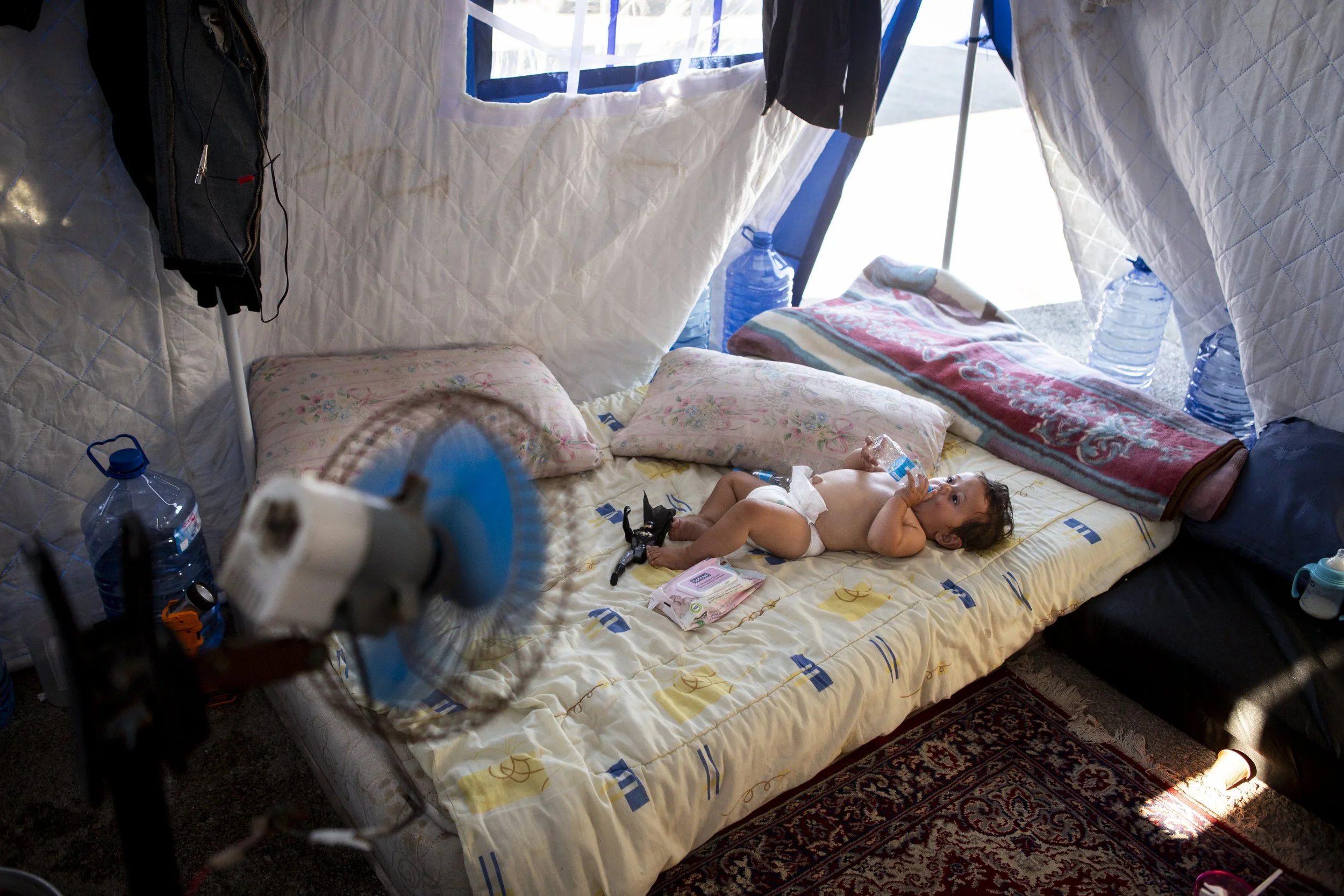 In their tent, Fatme and Jamal care for their neighbour’s young son. The extreme heat has left the boy severely distressed: hours of nonstop crying and violent coughing have increased the pressure on his abdomen so much that his belly button has prot