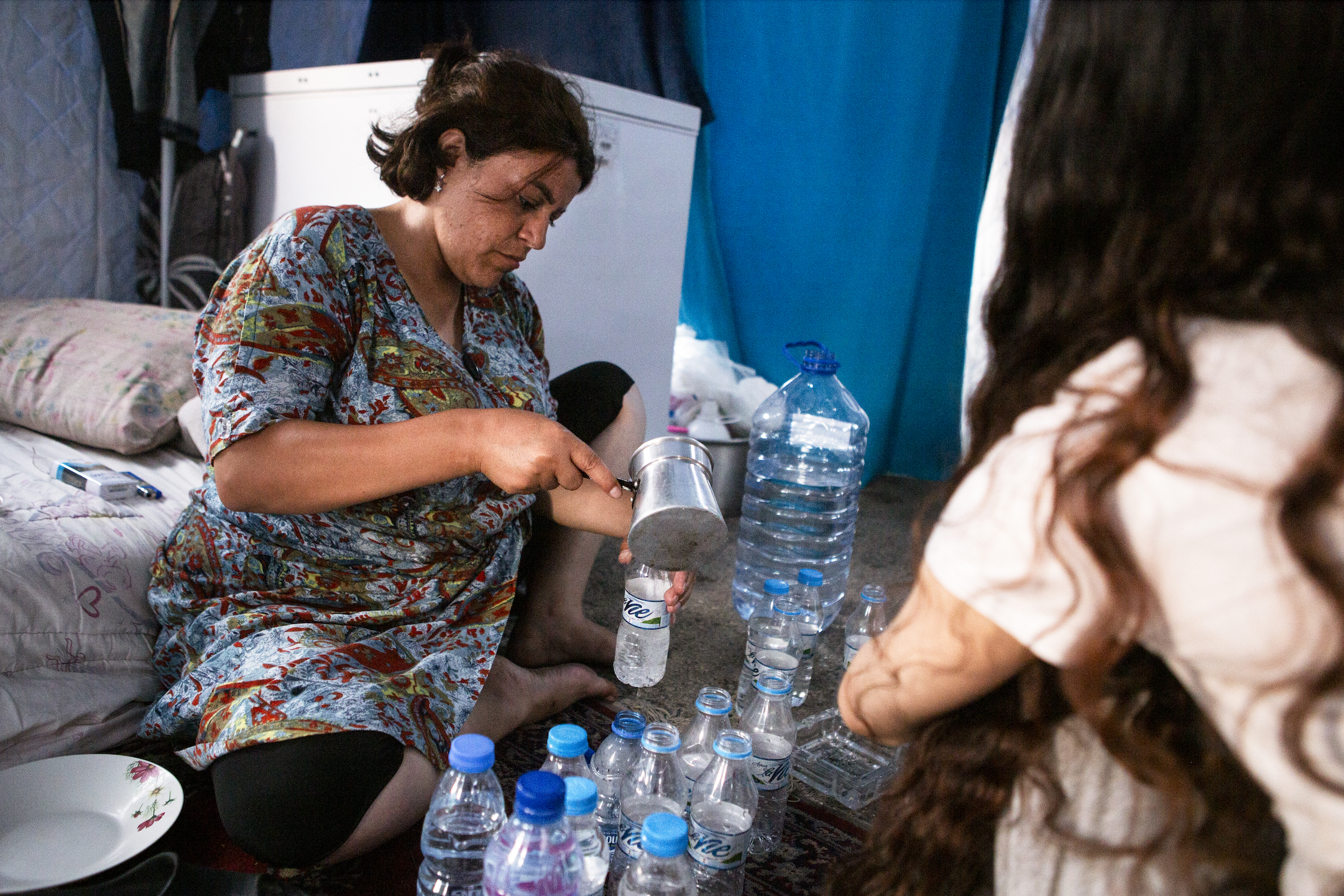 Fatme pours water into a small plastic bottle, which she will place inside the freezer container her husband brought to their tent. The container is used to store cold drinks — not just for their own family, but for others living in the camp as well.