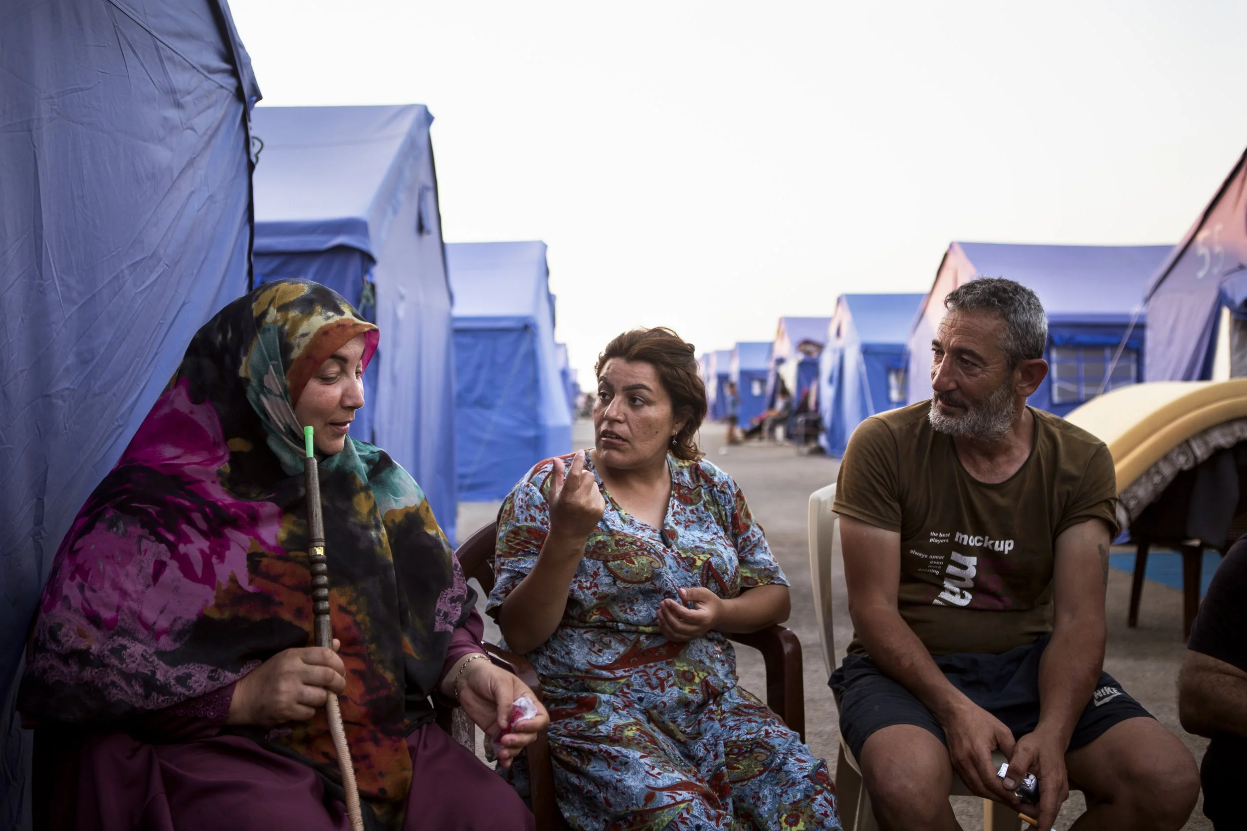 Fatme and her husband Jamal speak with their neighbour on the ground in between tents in the afternoon. 
