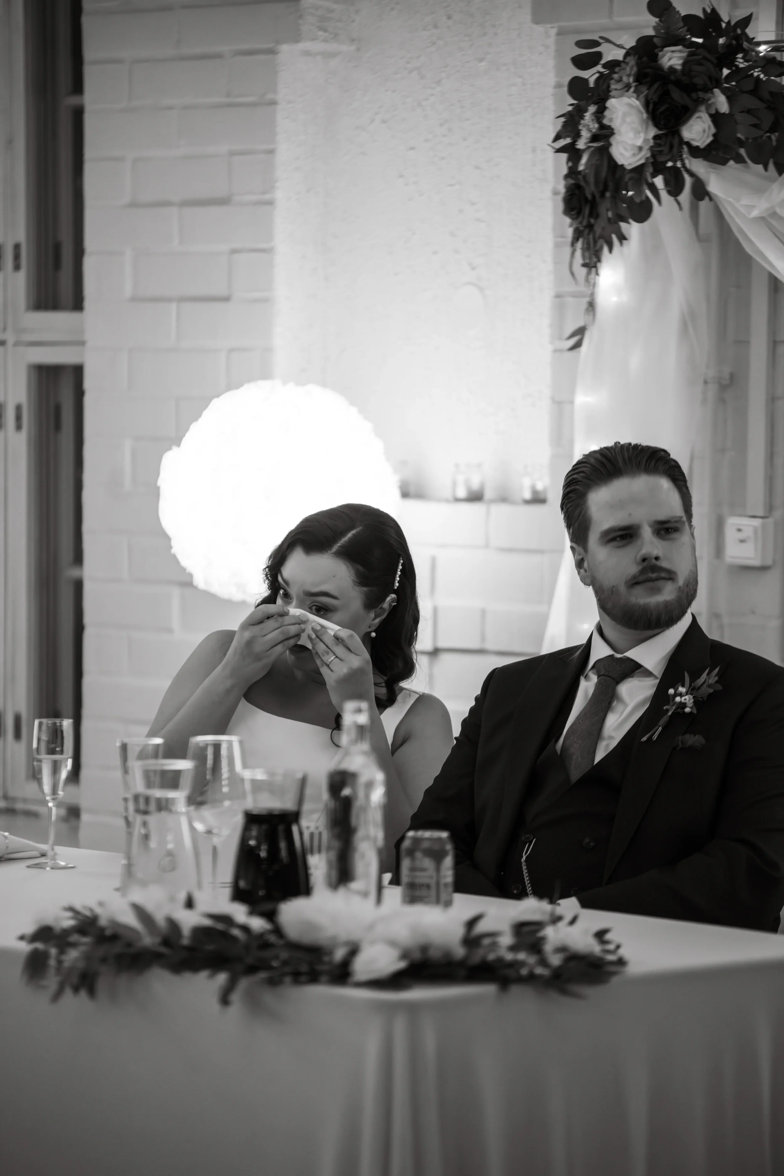 Mies ja nainen istuvat juhlapöydässä, nainen itkee ja pitelee nenäliinaa, mies katsoo poispäin. Hääkuvaaja Tampere.