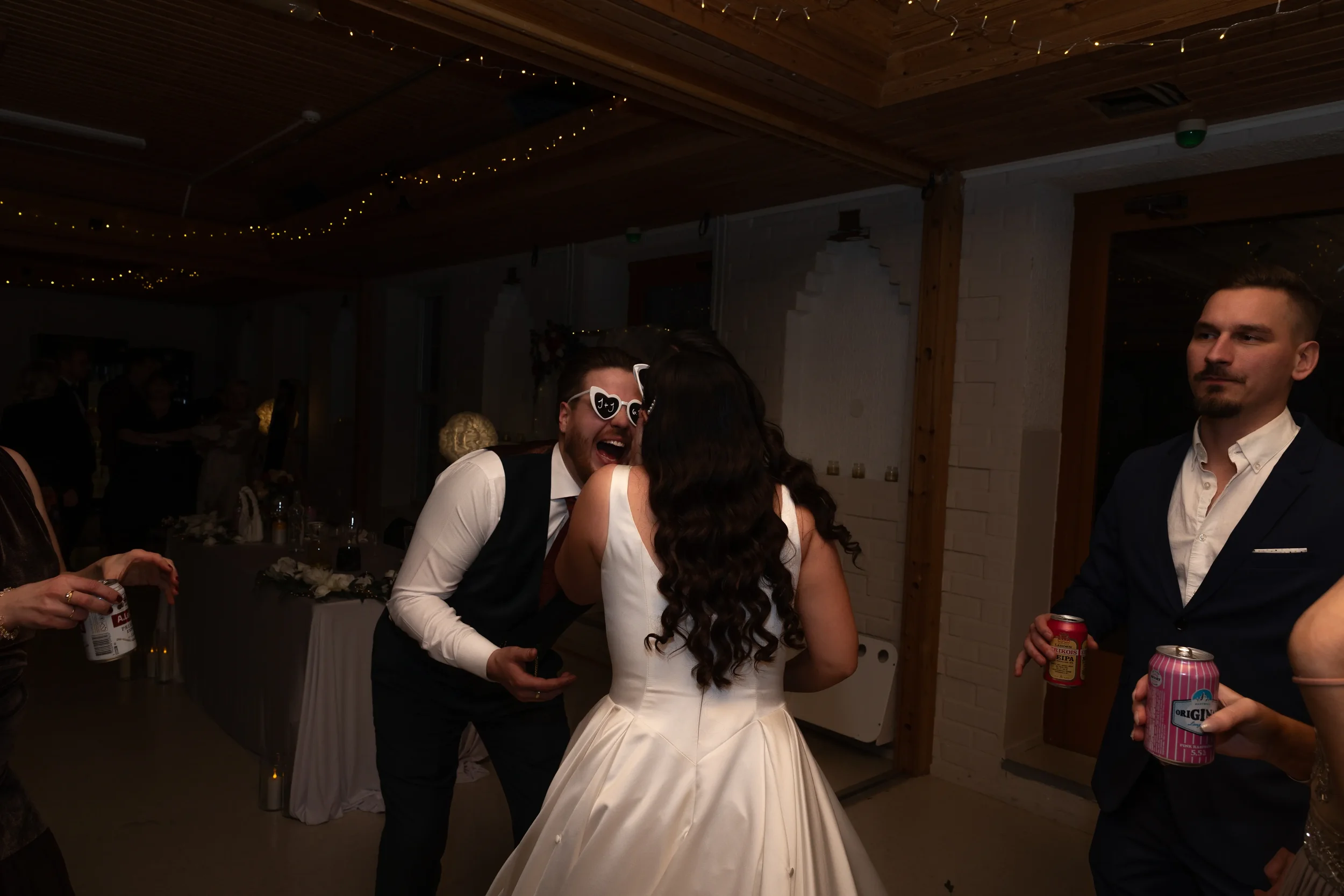 Hääpari ja vieraat tanssimassa juhlassa sisätiloissa, tunnelmavalot ja koristeet näkyvissä. Hääkuvaus Tampere.