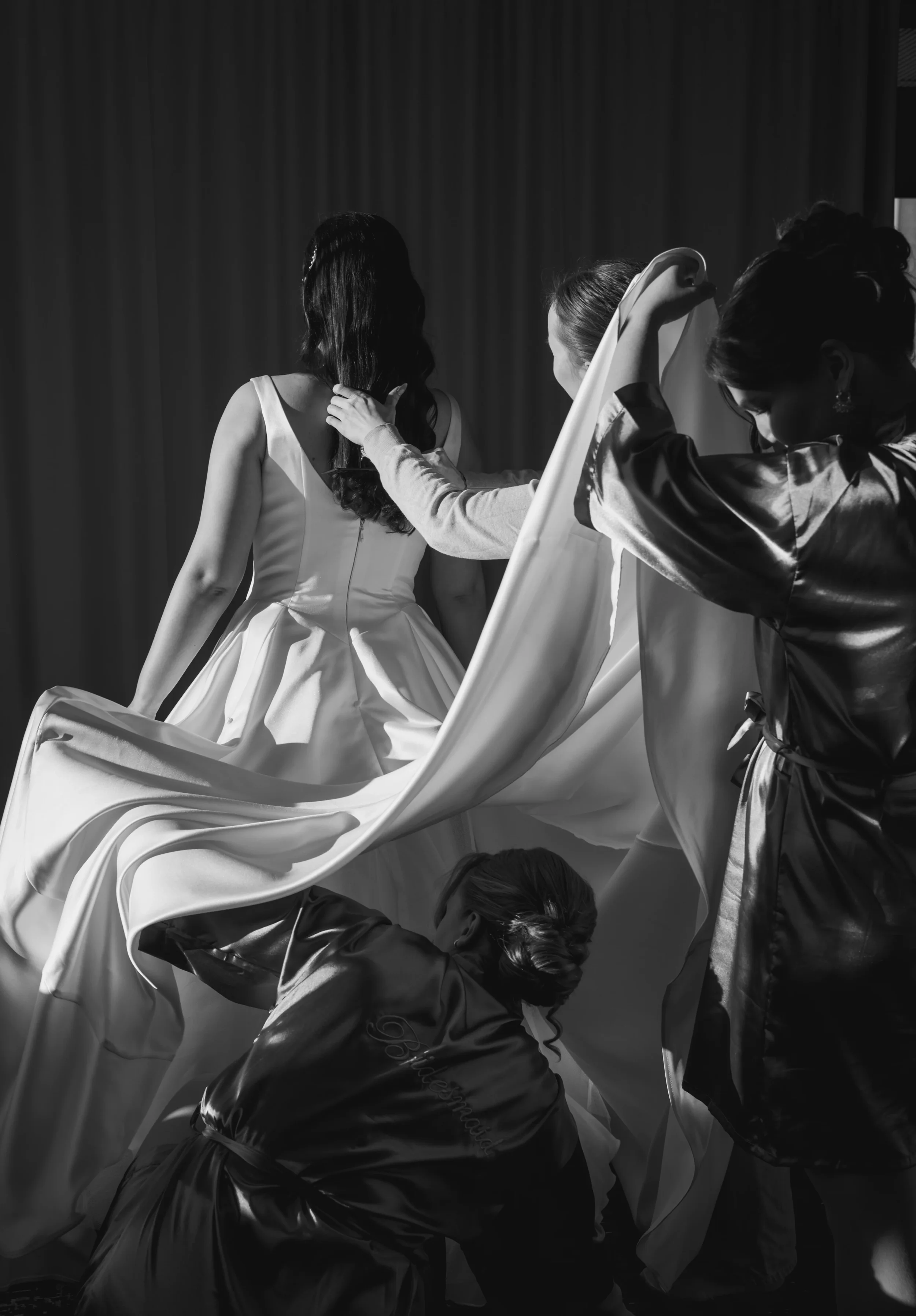 Morsian puetaan valkoiseen hääpukuun. Kaasot auttavat pukeutumisessa, mustavalkoinen kuva. Hääkuvaaja Tampere.