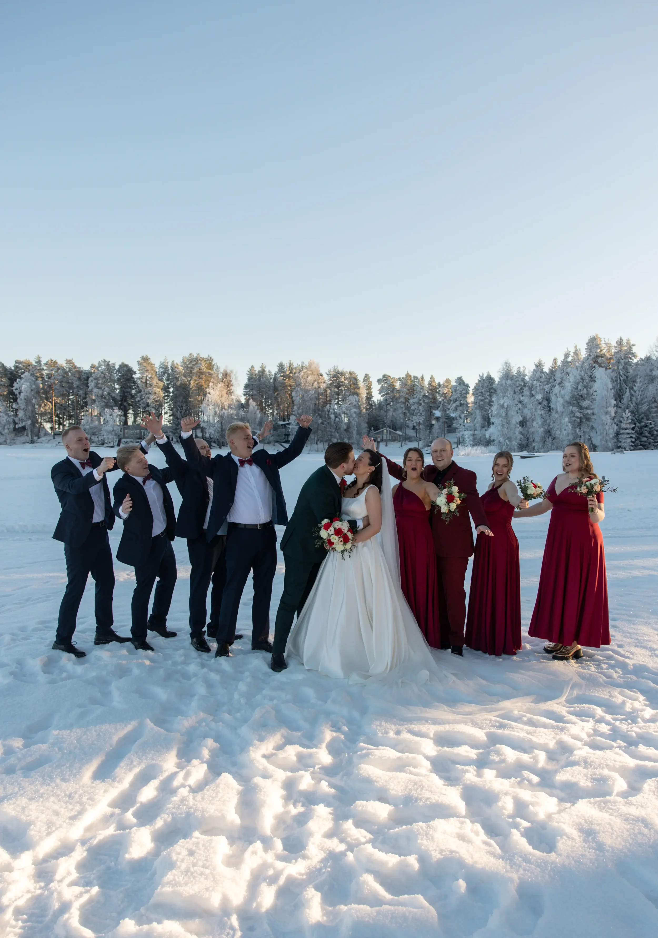 Hääpari kuvassa kaasojen ja bestmanien kanssa, jotka hurraavat. Kuva otettu järvenjäällä talvisessa maisemassa. Hääkuvaaja Tampere.