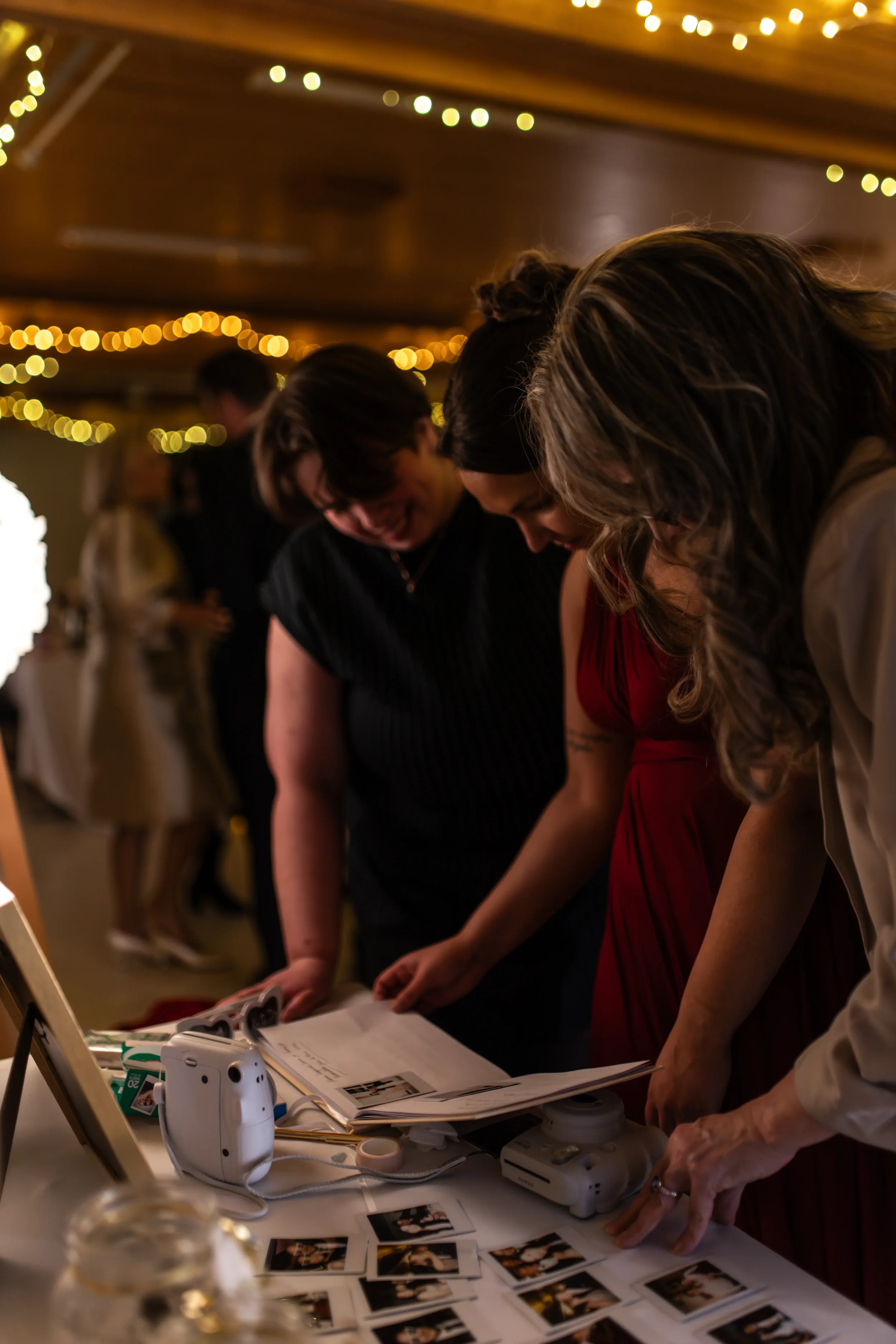 Kolme ihmistä katsoo vieraskirjaa, jossa on valokuvia ja terveisiä. Taustalla on sisätiloissa koristeltu juhlatunnelma. Hääkuvaus Tampere.