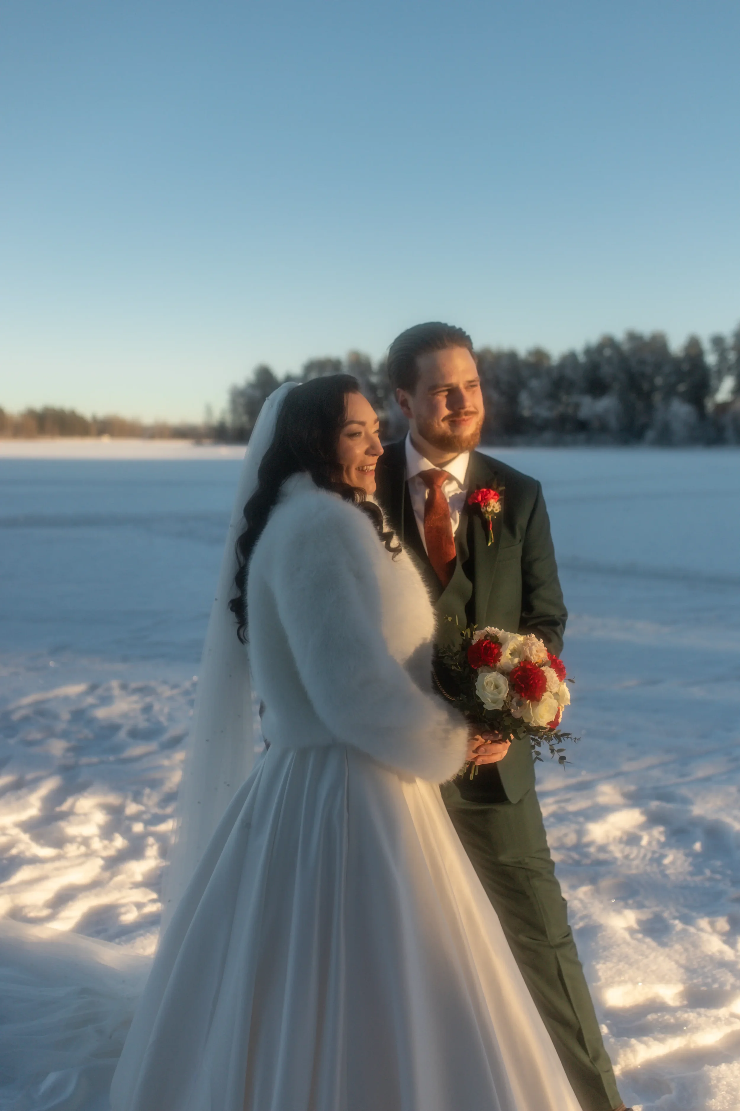 Hääpari seisoo järven jäällä, taustalla talvimaisema ja selkeä taivas. Hääkuvaaja Tampere.