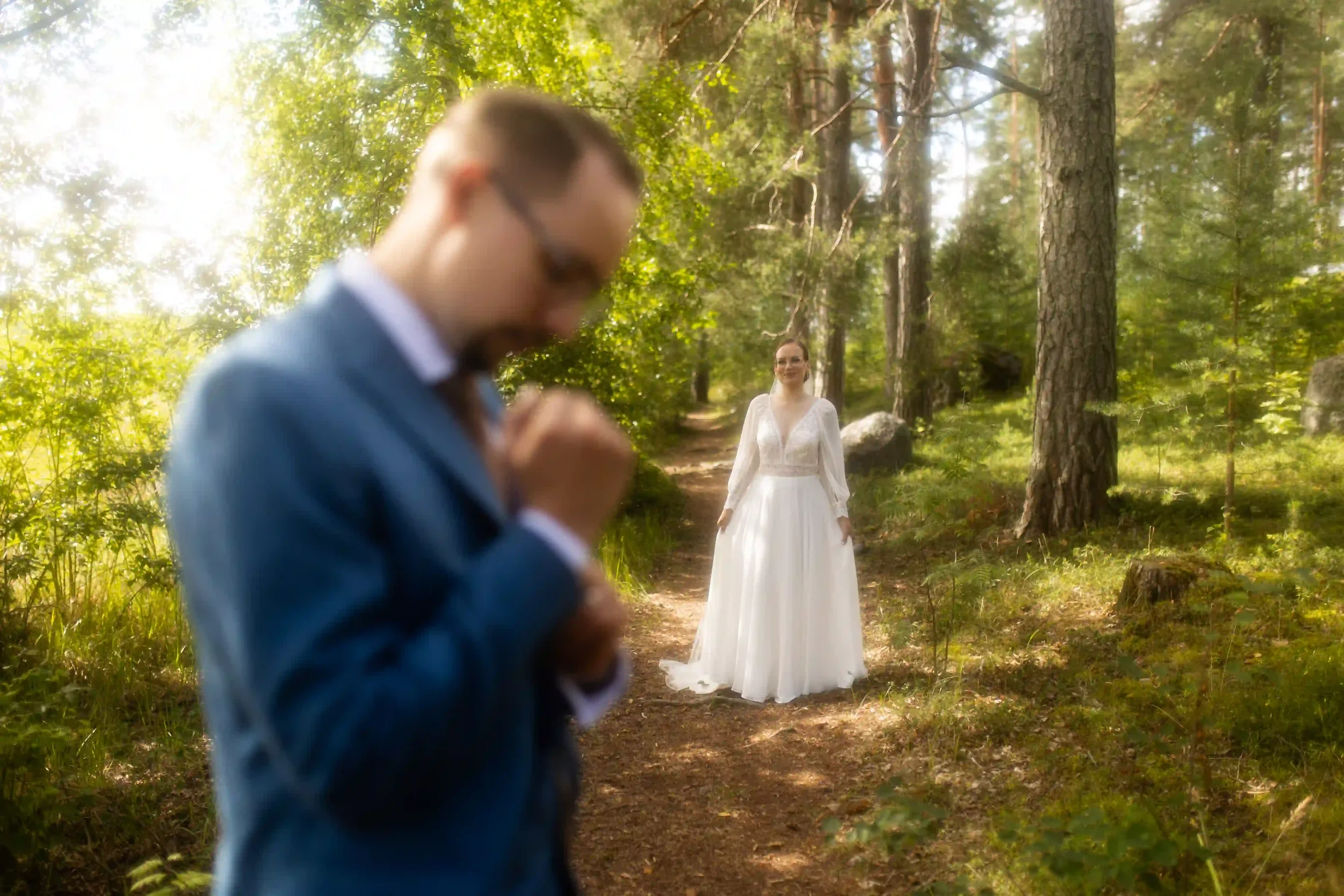 Kuva hääparista metsässä, mies on melkein kokonaan näkyvissä ja nainen seisoo polulla taustalla, ympäröivässä luonnossa.