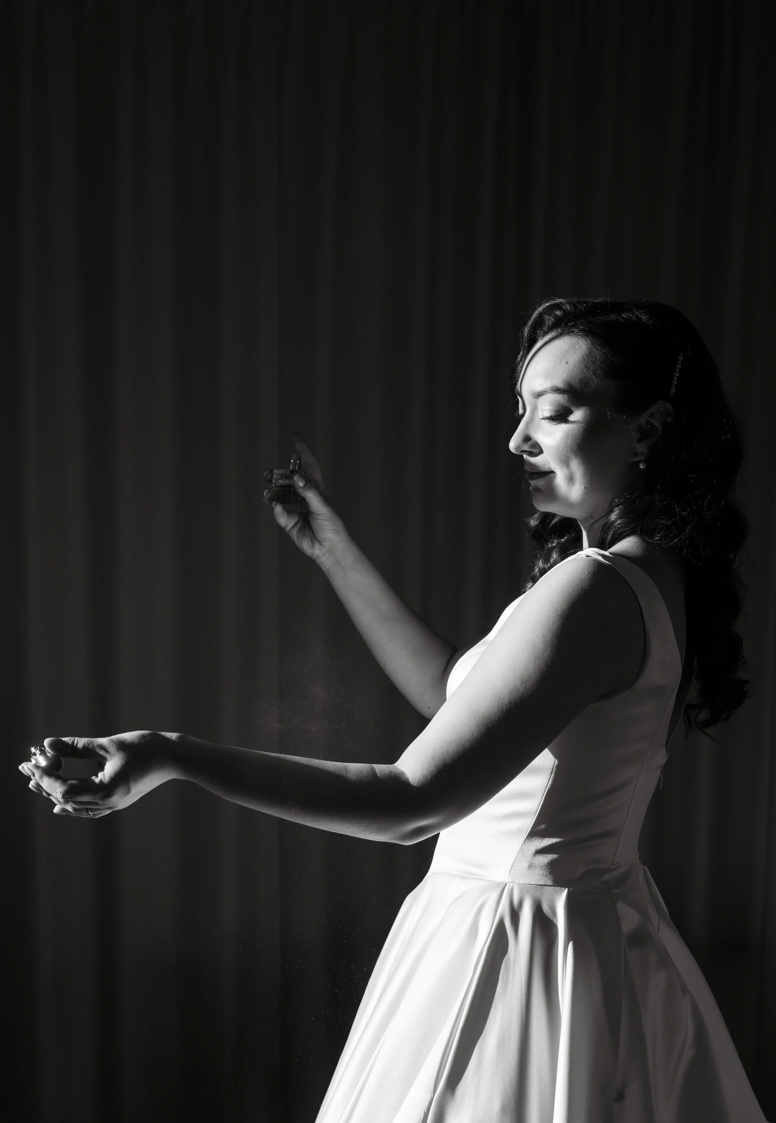 Mustavalkoinen kuva morsiamesta joka suihkuttaa hajuvettä auringon valossa. Hääkuvaaja Tampere.