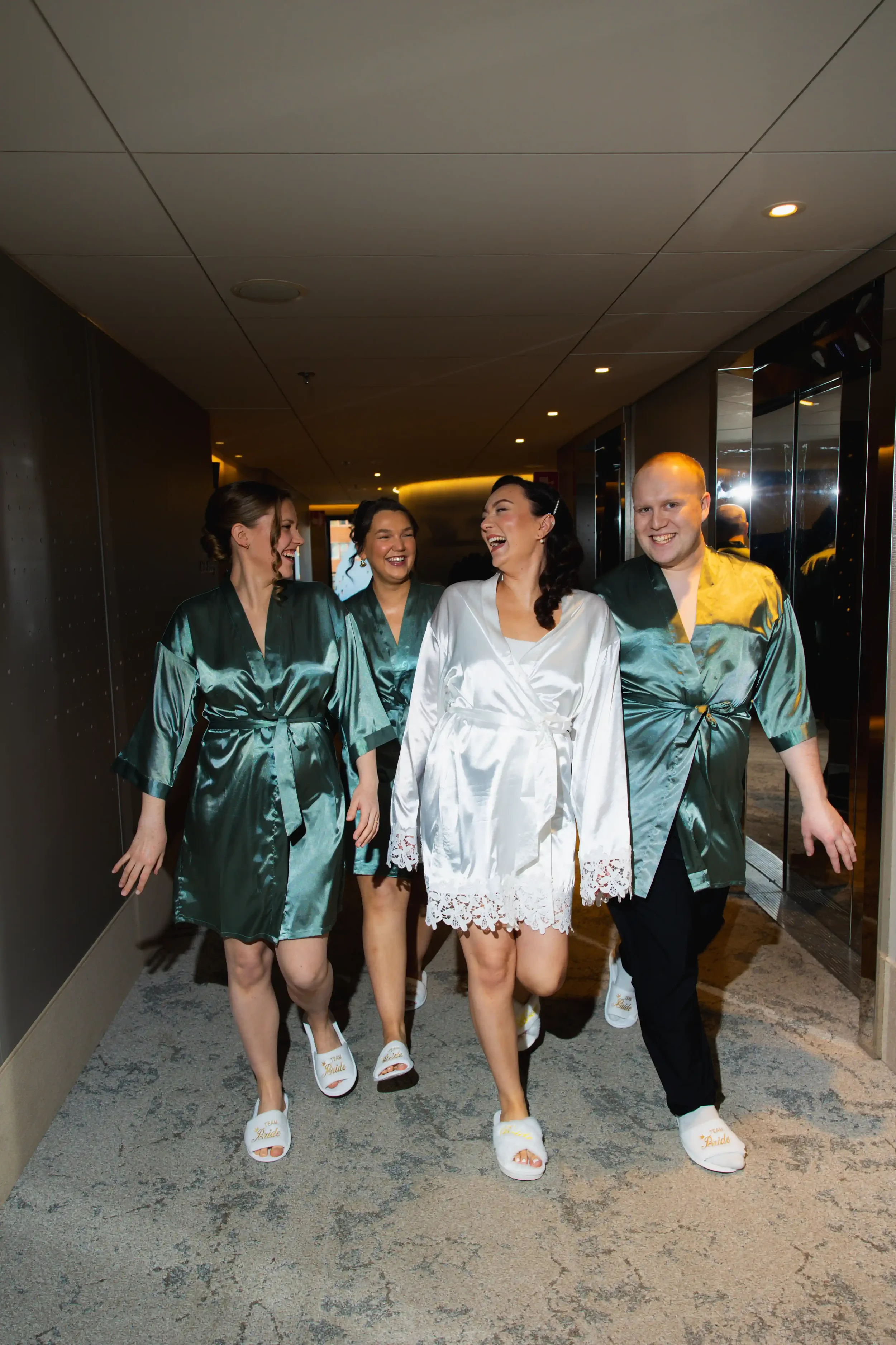 Kuvassa neljä ihmistä pukeutuneena silkkitakkeihin ja kävelemässä käytävää. Hääkuvaaja Tampere.