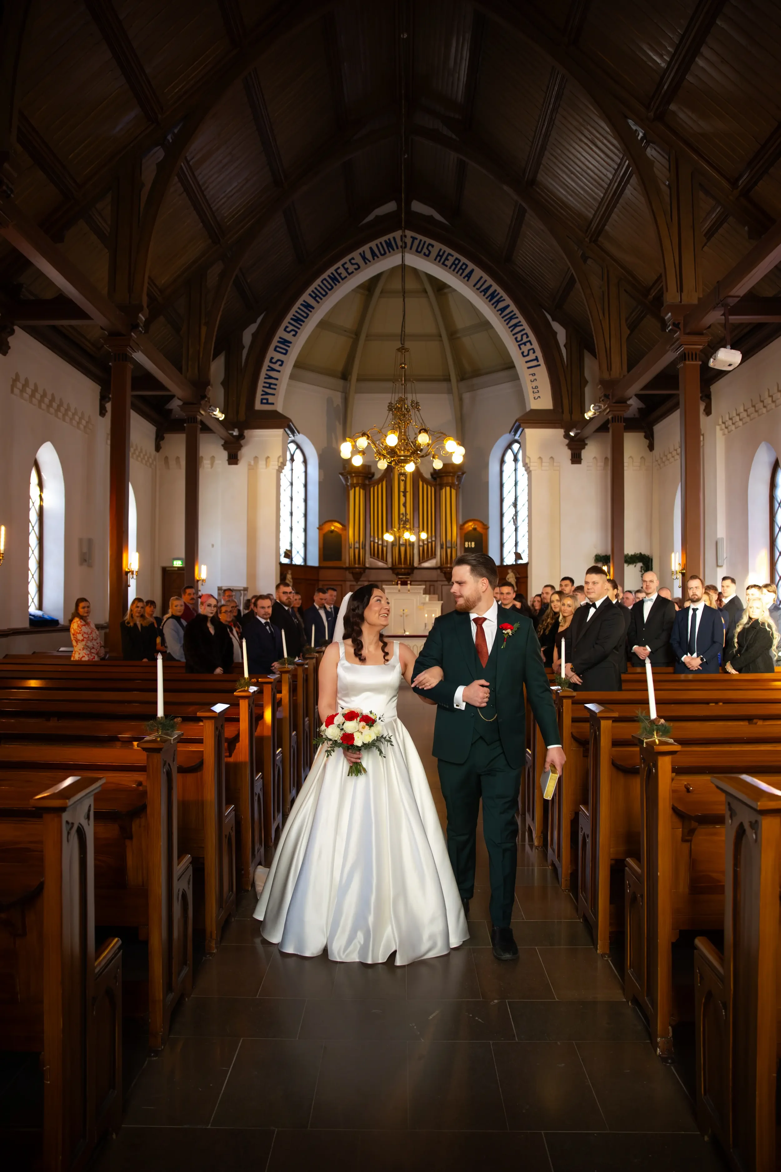 Hääpari kävelee kirkossa, nainen häämekossaan ja mies puvussa, ystävät ja vieraat katsovat. Hääkuvaaja Tampere.