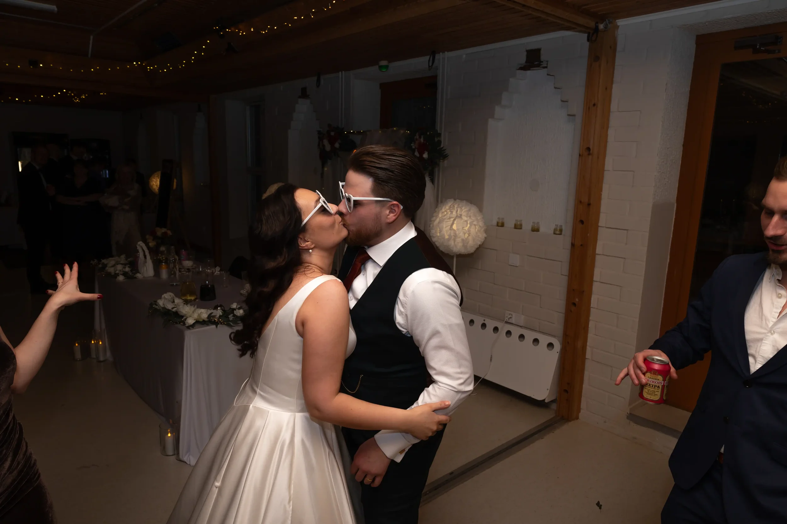 Hääpari suutelee toisiaan tanssilattialla, vieraat katsovat ja juovat, tunnelmallinen valaistus. Hääkuvaus Tampere.