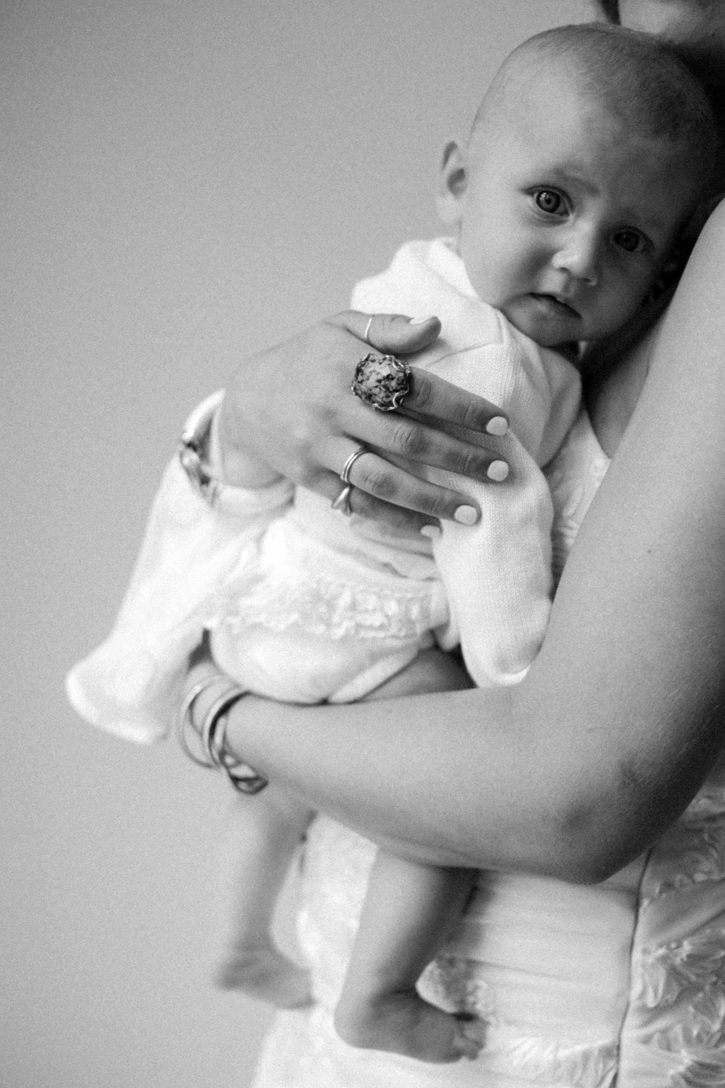 A woman holding a baby close to her chest, with the baby's face visible and looking at the camera. The photo is in black and white.