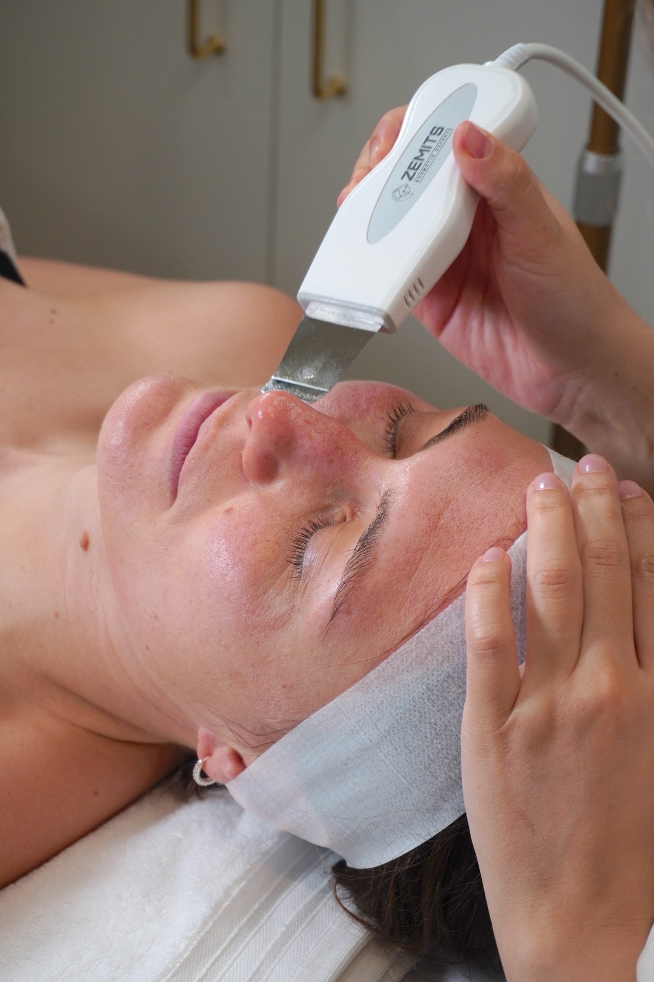 A woman receiving a facial treatment using a handheld device in a spa or clinic setting.