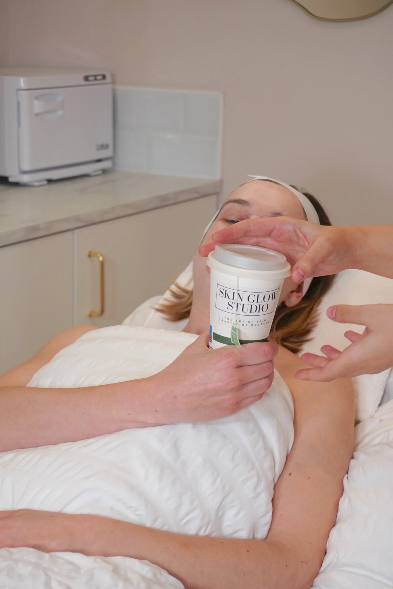 A woman lying in bed receiving a skincare treatment with a product from Skin Glow Studio.