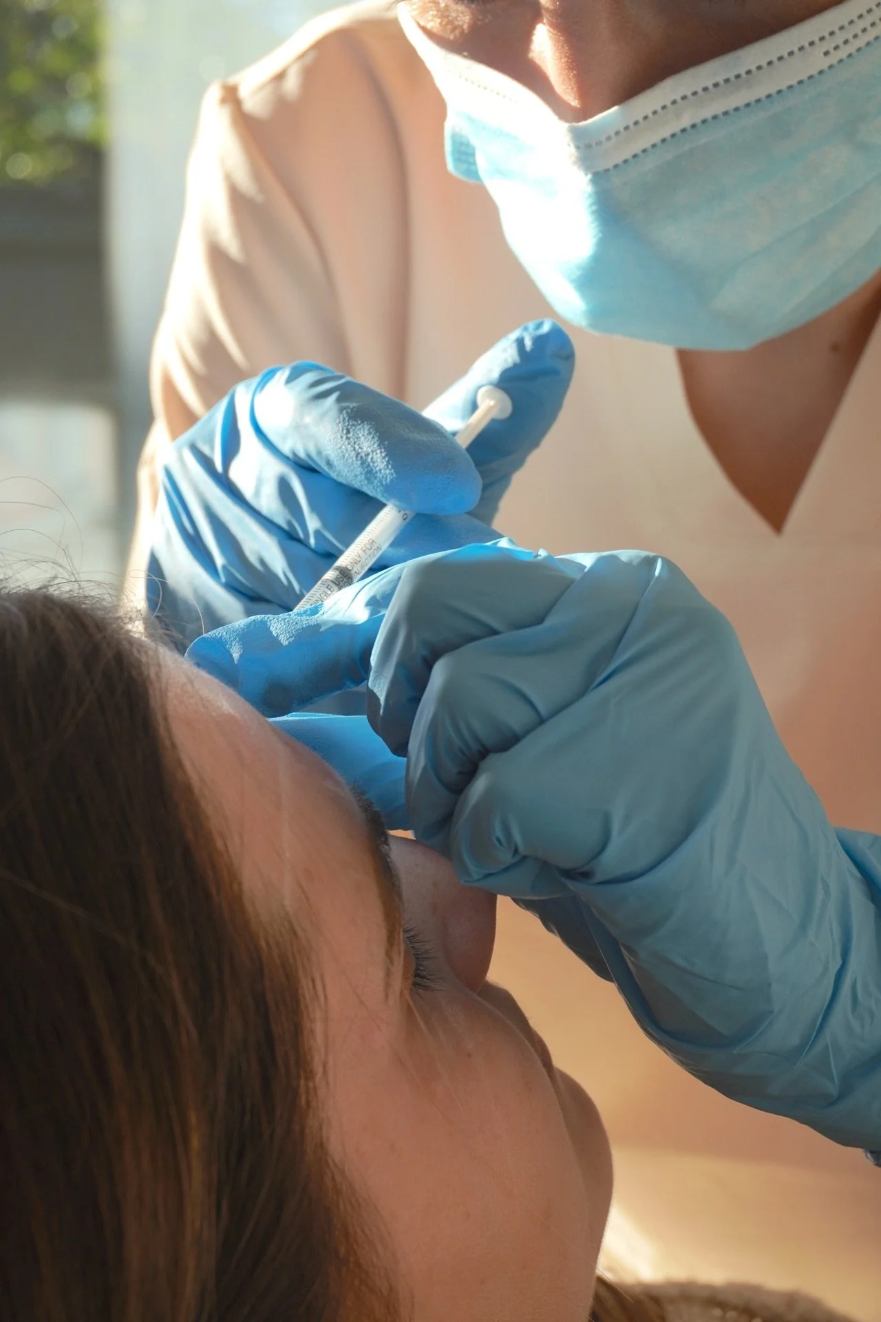 A healthcare worker gives a vaccination to a woman, wearing gloves and a face mask.