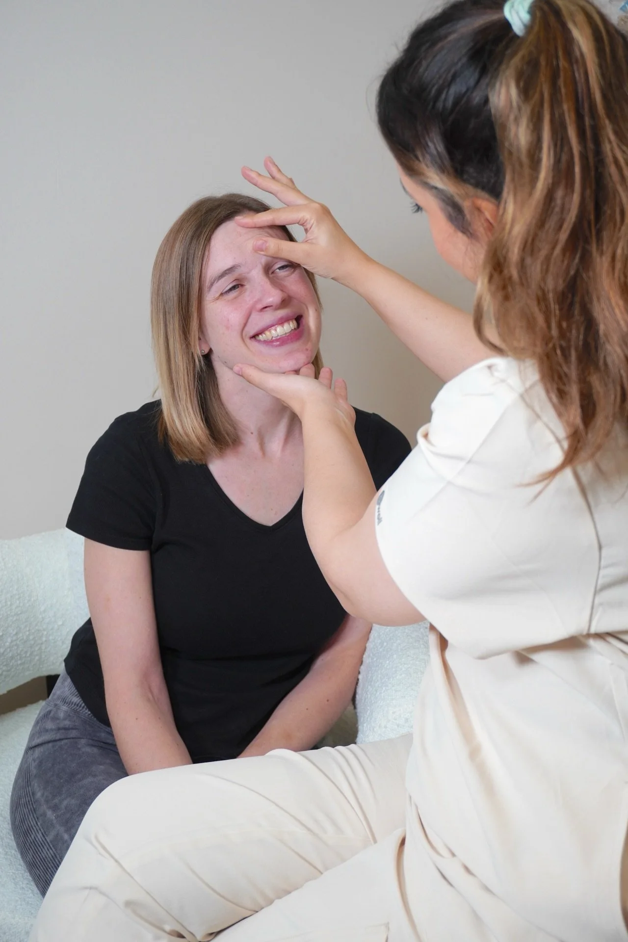 A medical professional examines a woman who appears to be upset or distressed, touching her forehead and chin in a comforting manner.