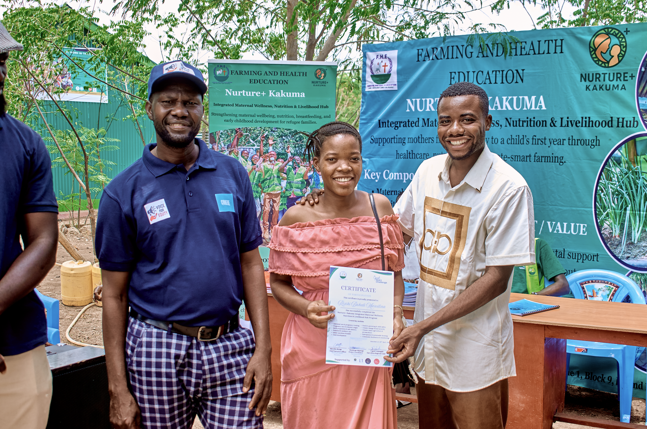 A woman receiving a certificate from a man at an outdoor event focused on farming and health education, with banners and people in the background.