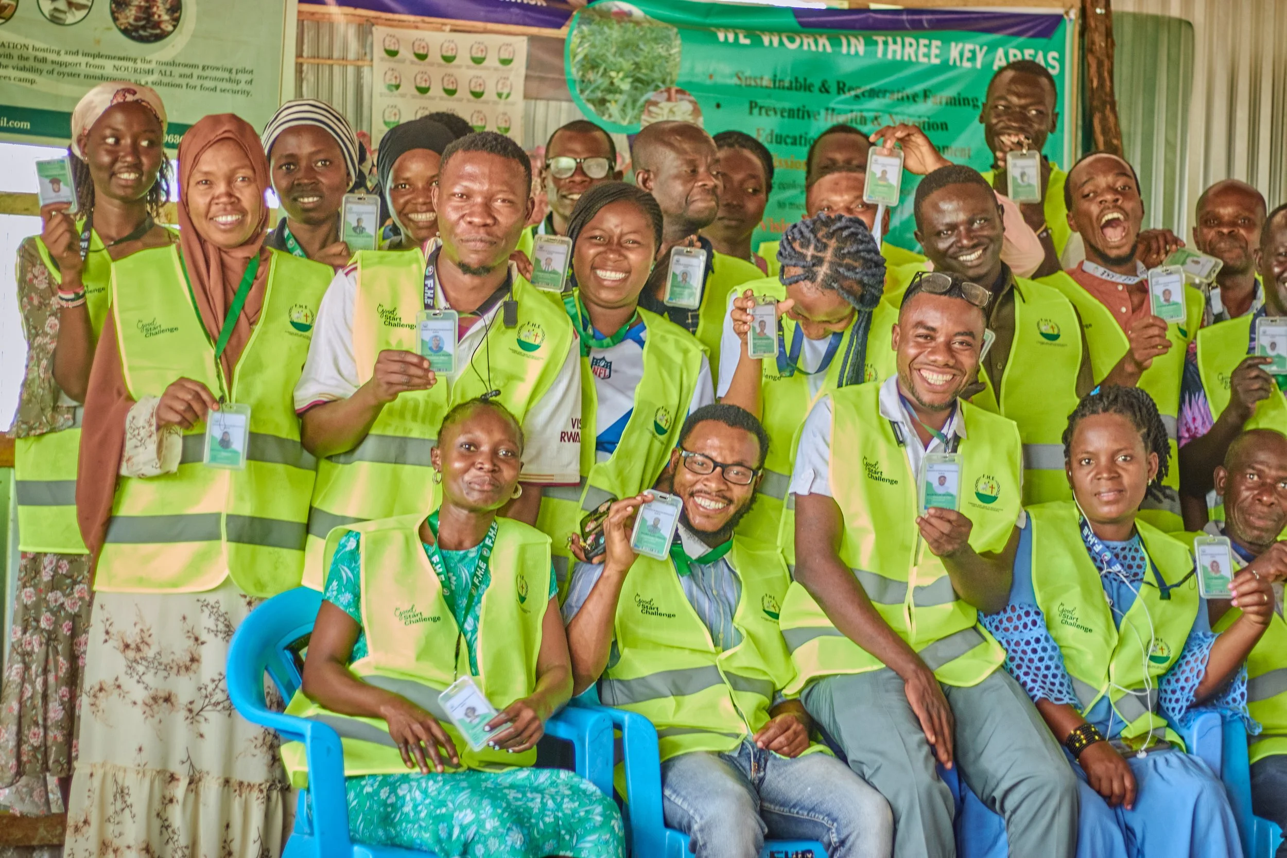 A diverse group of smiling people wearing neon yellow vests, holding identification cards, at an indoor event promoting sustainability and environmental awareness.
