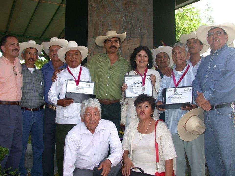Grupo de personas en una ceremonia de reconocimiento, con algunos mostrando diplomas y medallas, en un ambiente al aire libre.