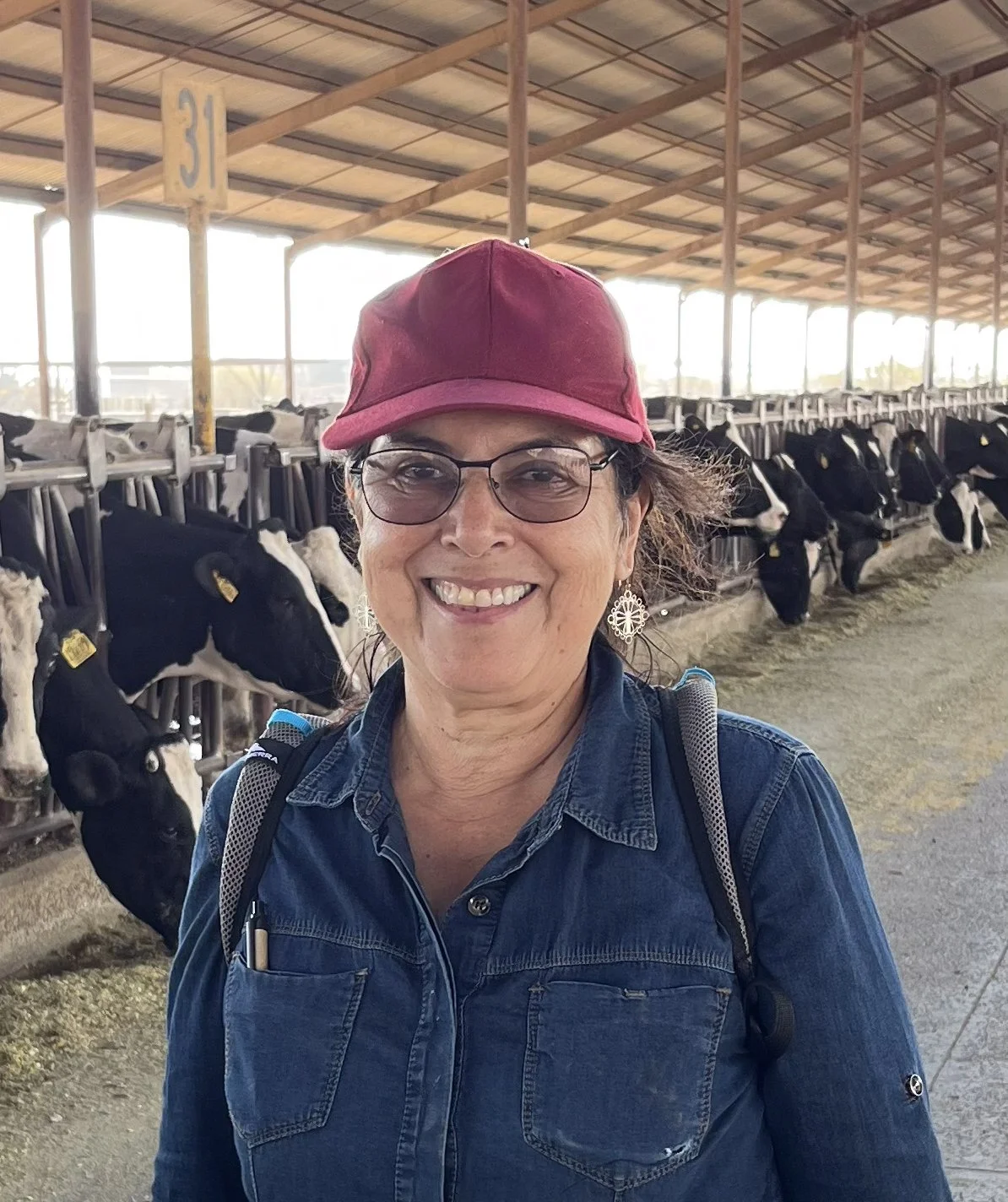Mujer sonriendo en una granja, con vacas en un establo al fondo.