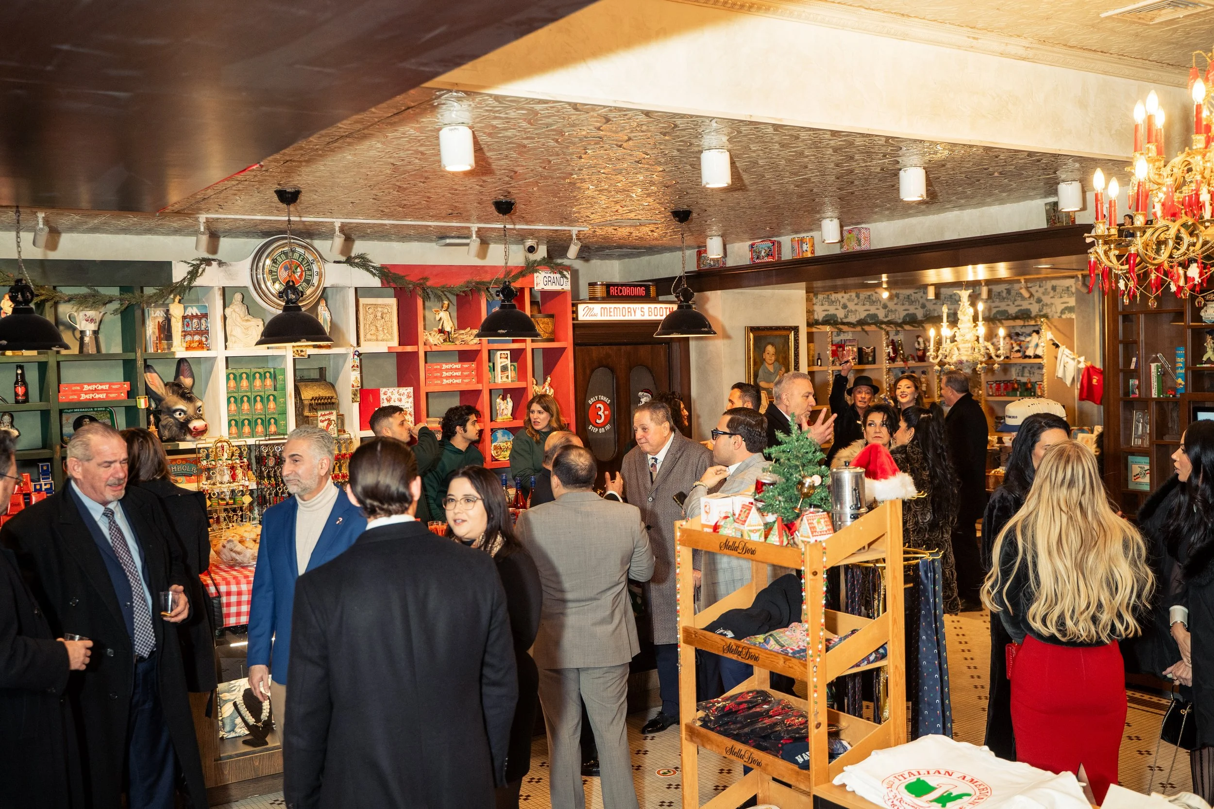 People gathered at a Christmas party in a decorated shop with shelves of holiday decorations and gifts, some wearing festive attire and Santa hats.