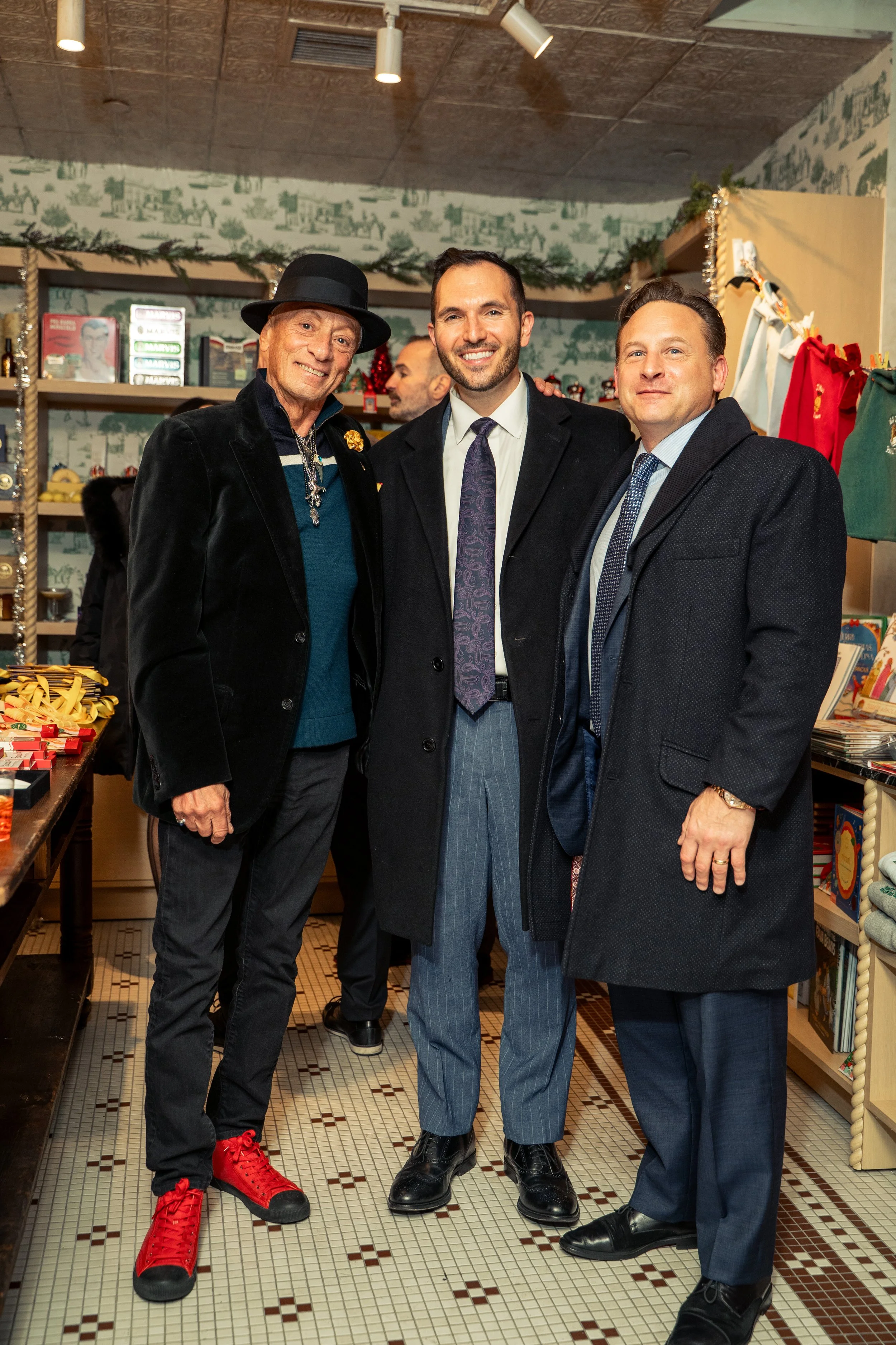 Three men standing together indoors, smiling at the camera, inside a shop decorated for Christmas.