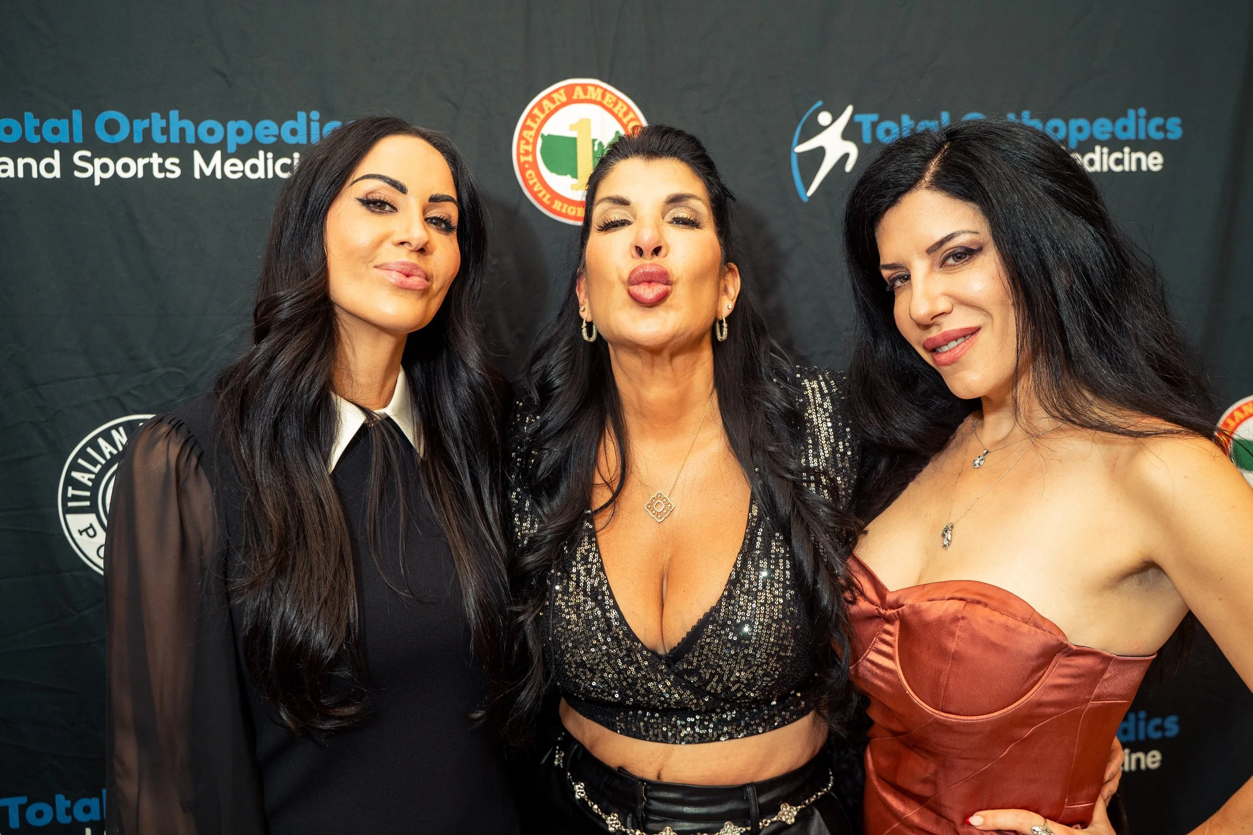 Three women posing together at an event, standing in front of a backdrop with medical logos and text.