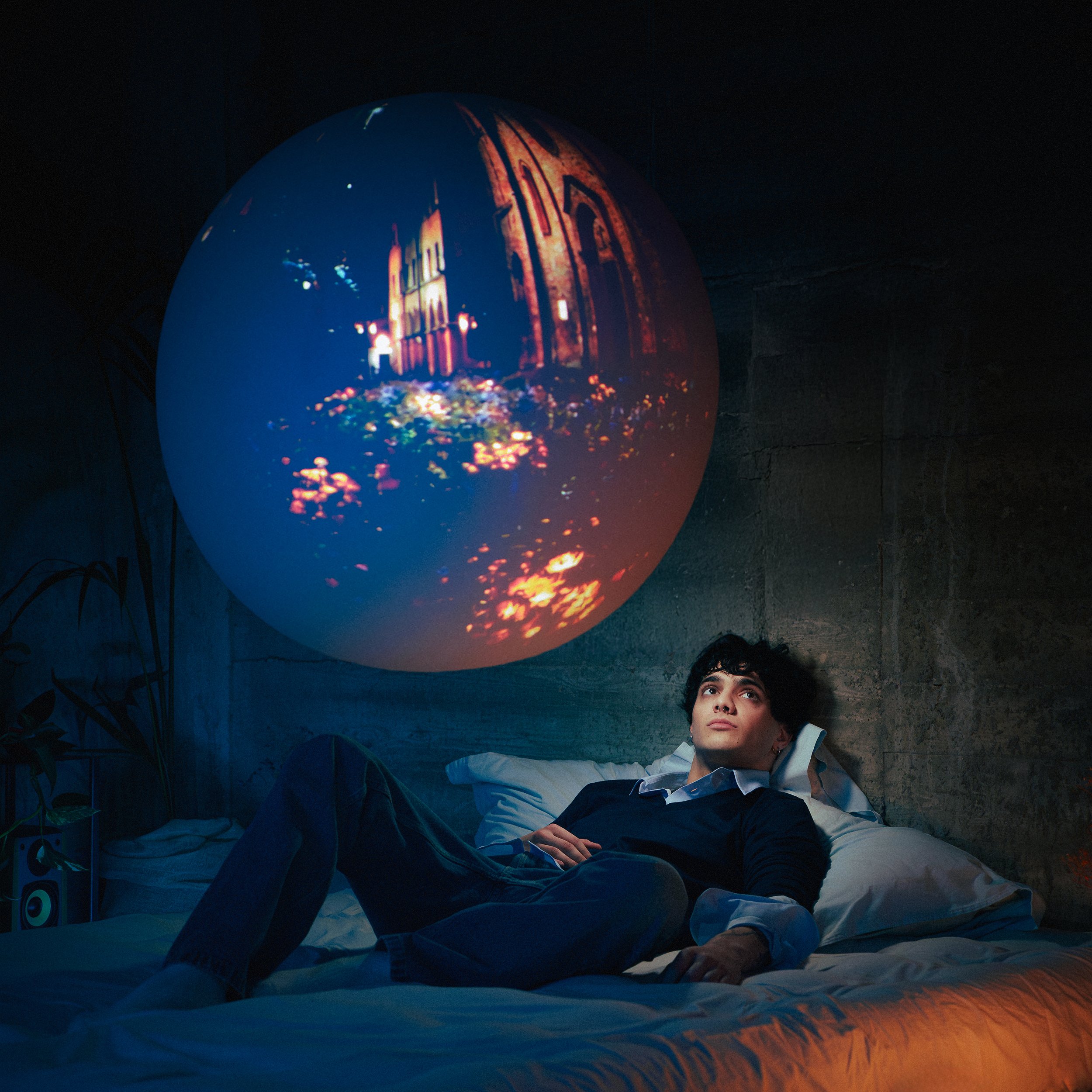 Un giovane uomo sdraiato in letto in una stanza buia guarda un proiettore di luci che mostra un'immagine di un edificio storico di notte.