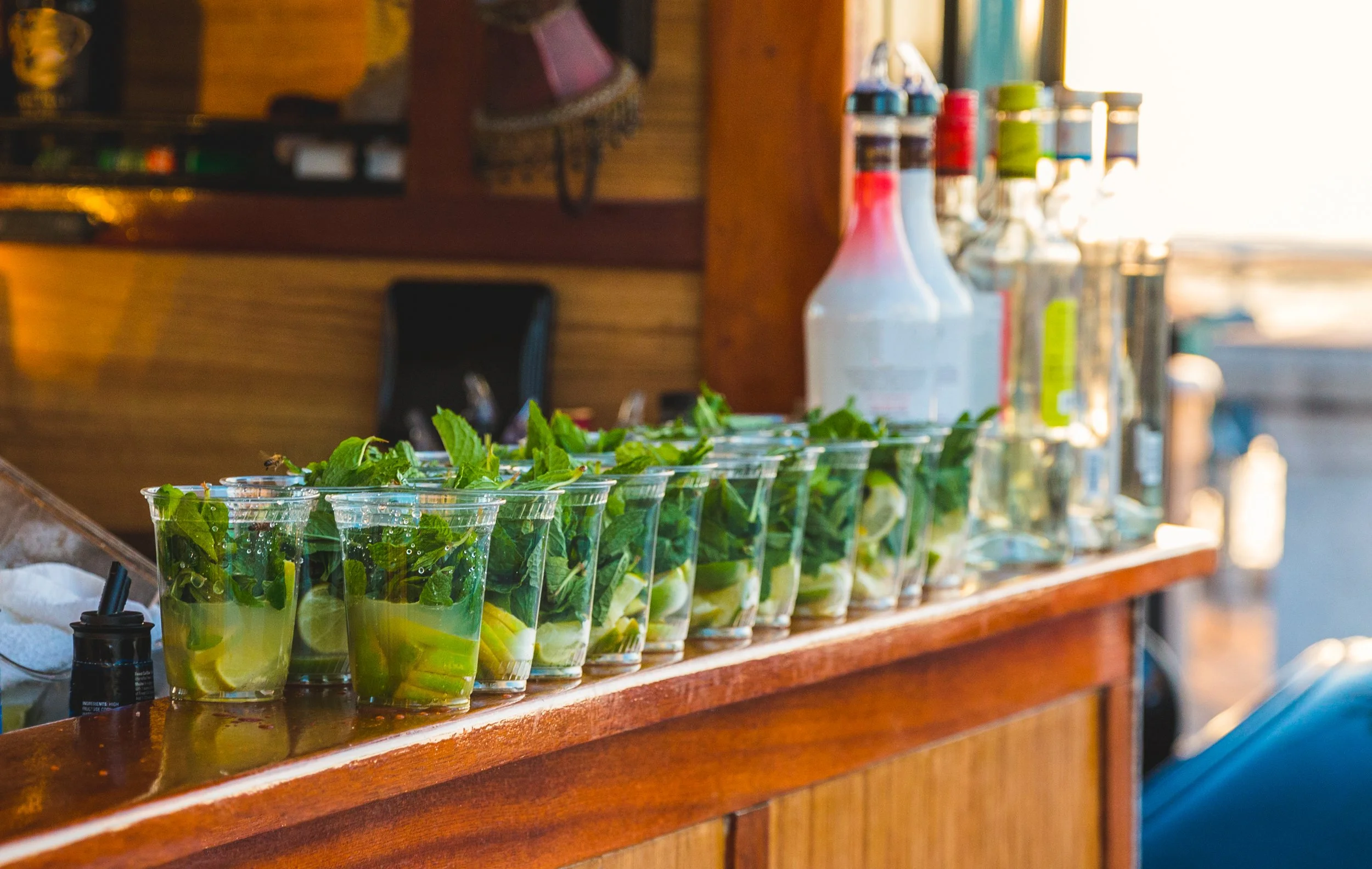 A regatta party with rows of mojito cocktails with mint leaves, lime slices, and ice on a mobile bar counter.