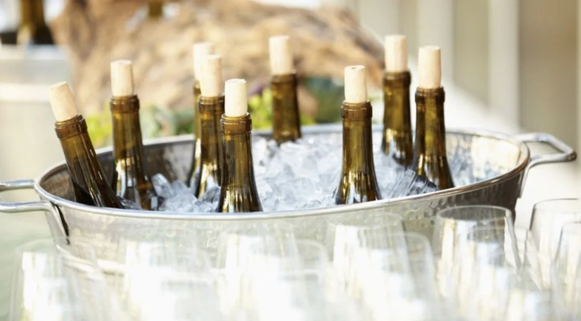 Bottles of wine and wine glasses chilling in an ice-filled silver metal tub ready for luxury event bar service. .