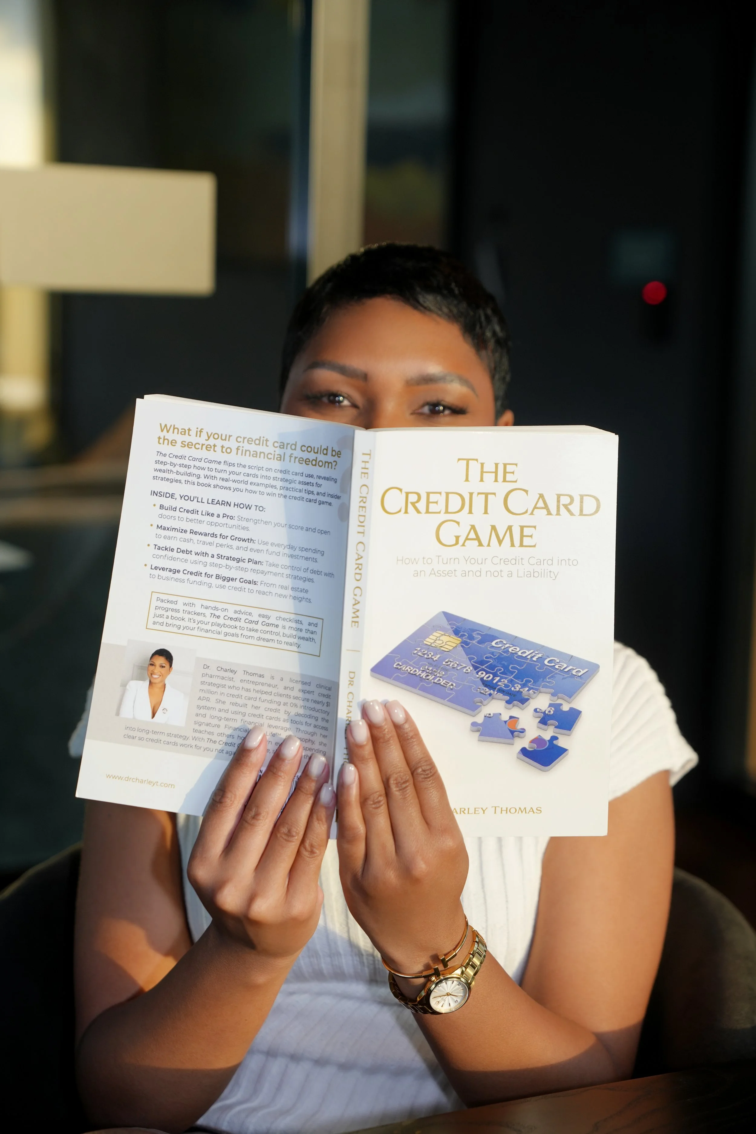 Dr. Charley holding book titled "The Credit Card Game" in front of her face, partially revealing her eyes.