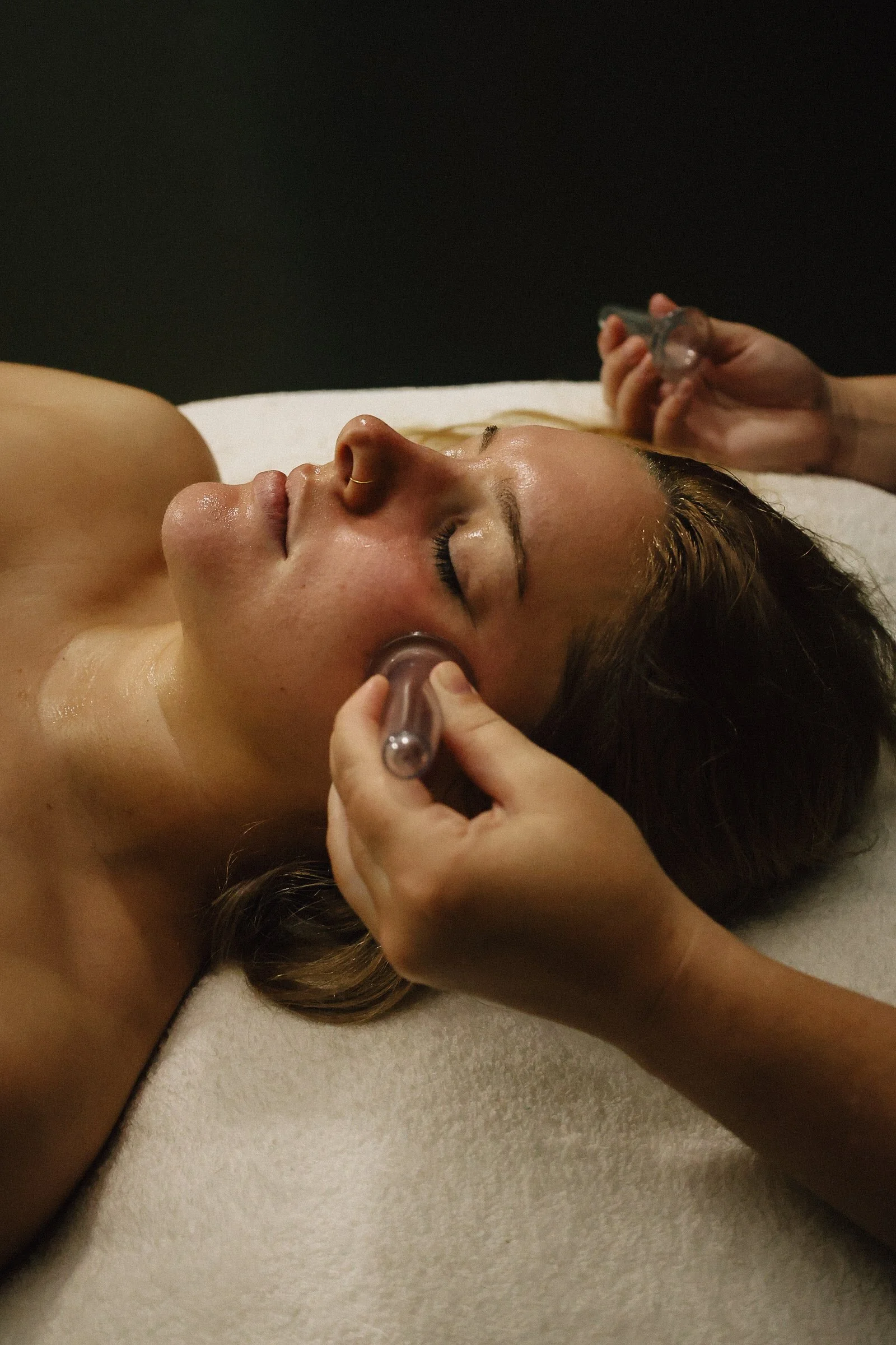 A woman receiving a facial massage with a facial roller in a spa setting.
