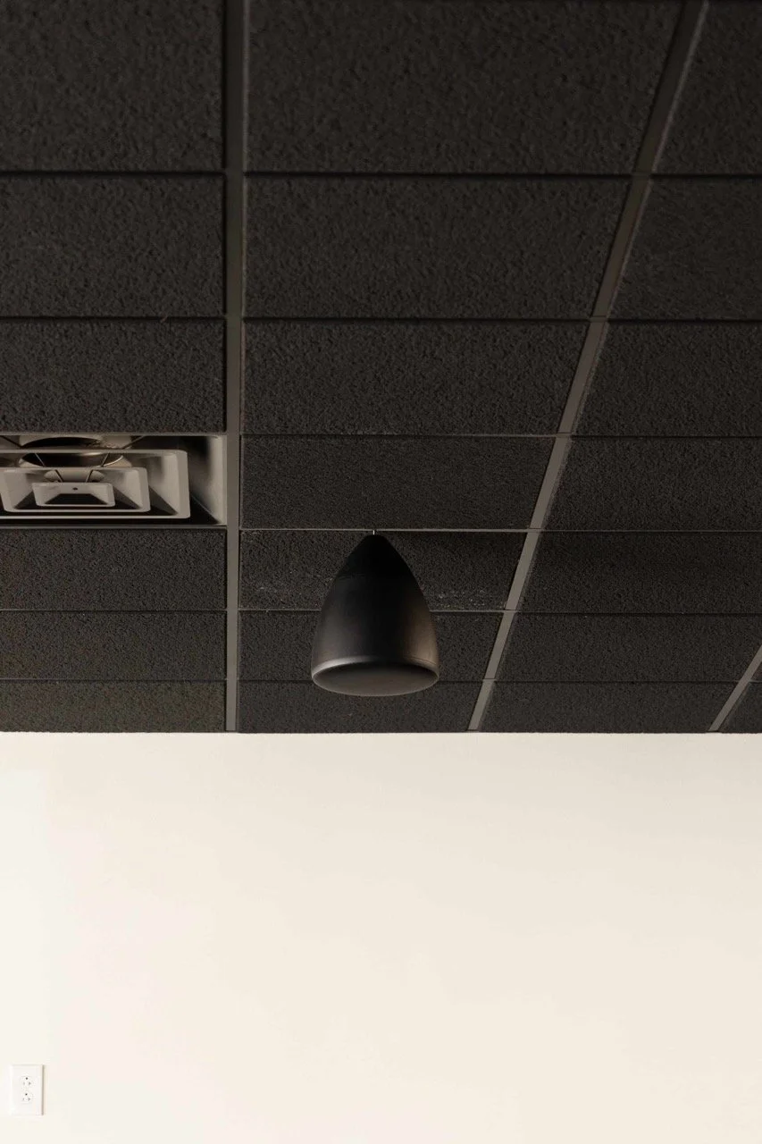 Commercial Audio & Video installation featuring a black speaker and air vent mounted on a grid-patterned ceiling in a business space.