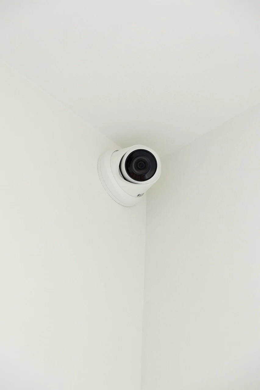 A white security camera mounted in the corner of a ceiling and wall.