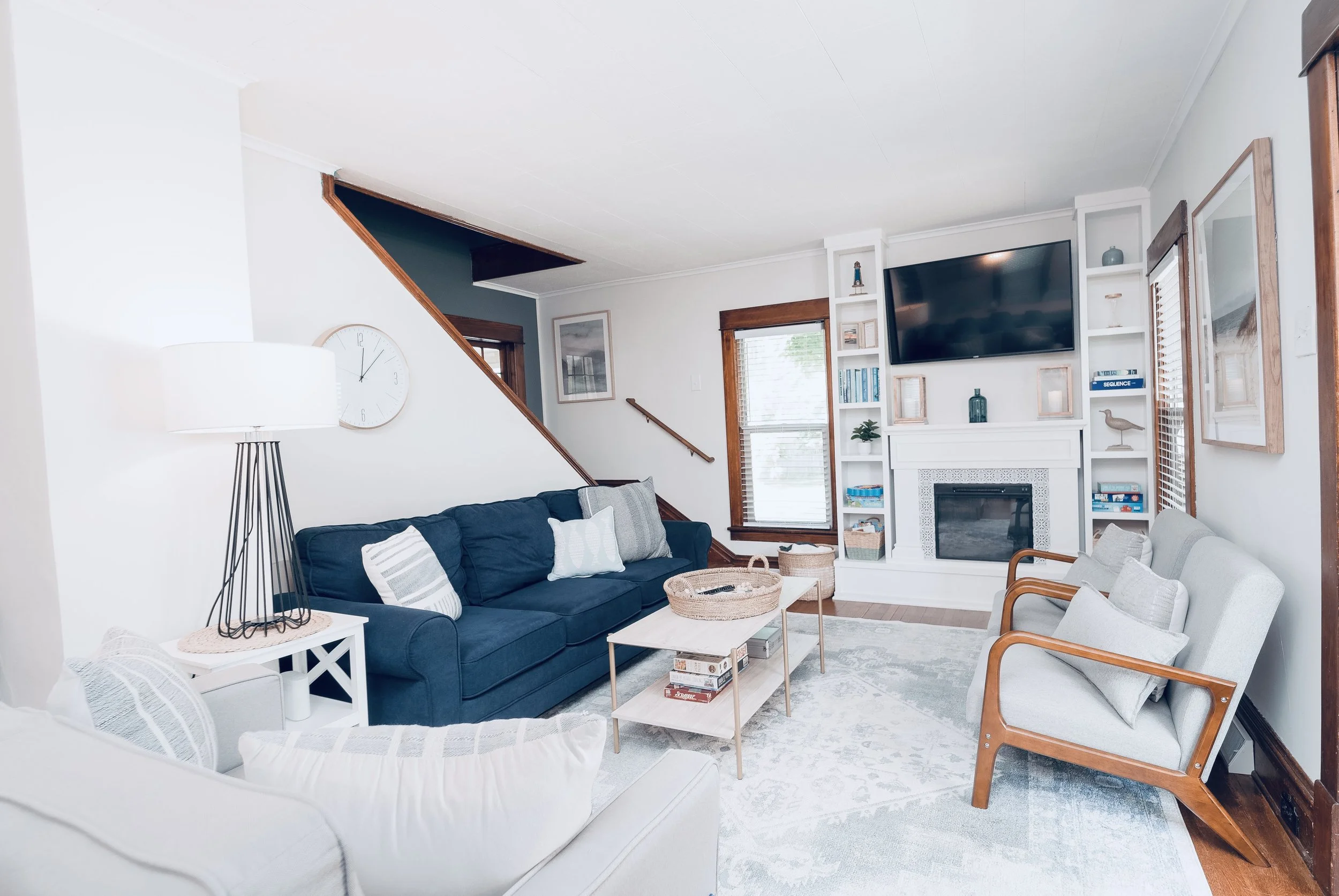 Living room with white and navy blue sofas, a white coffee table, a fireplace with built-in white shelves, a wall-mounted television, wooden window frames, and decorative pillows.