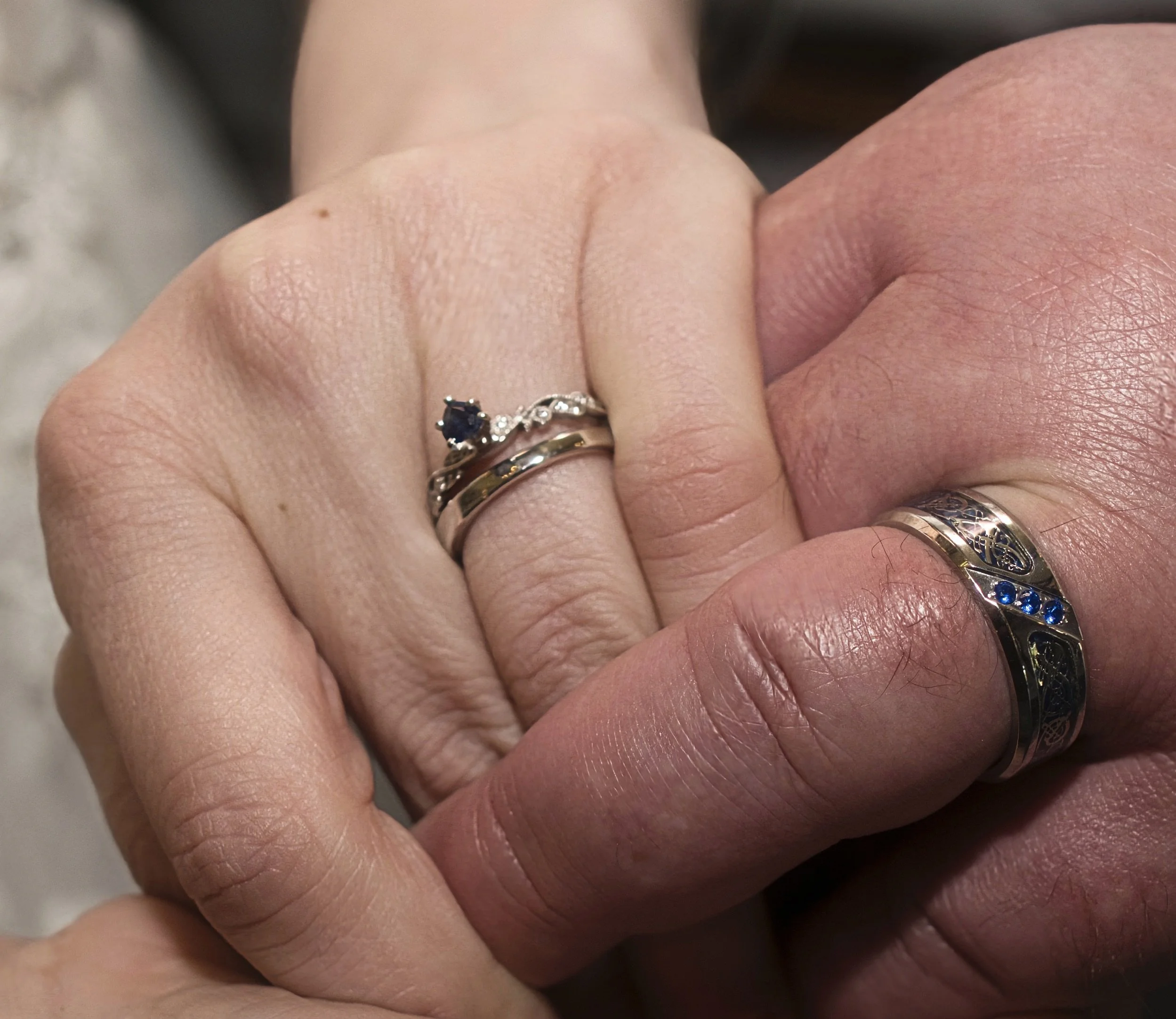 Close-up of a couple's hands clasped together, showing wedding and engagement rings on both rings.