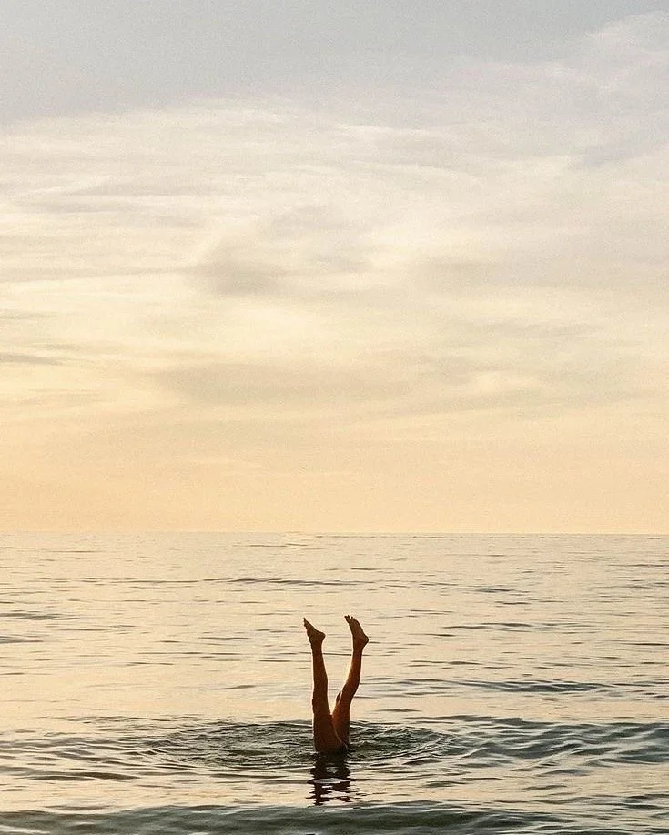 Person in the water doing a handstand with legs in the air during sunset or sunrise at the beach.