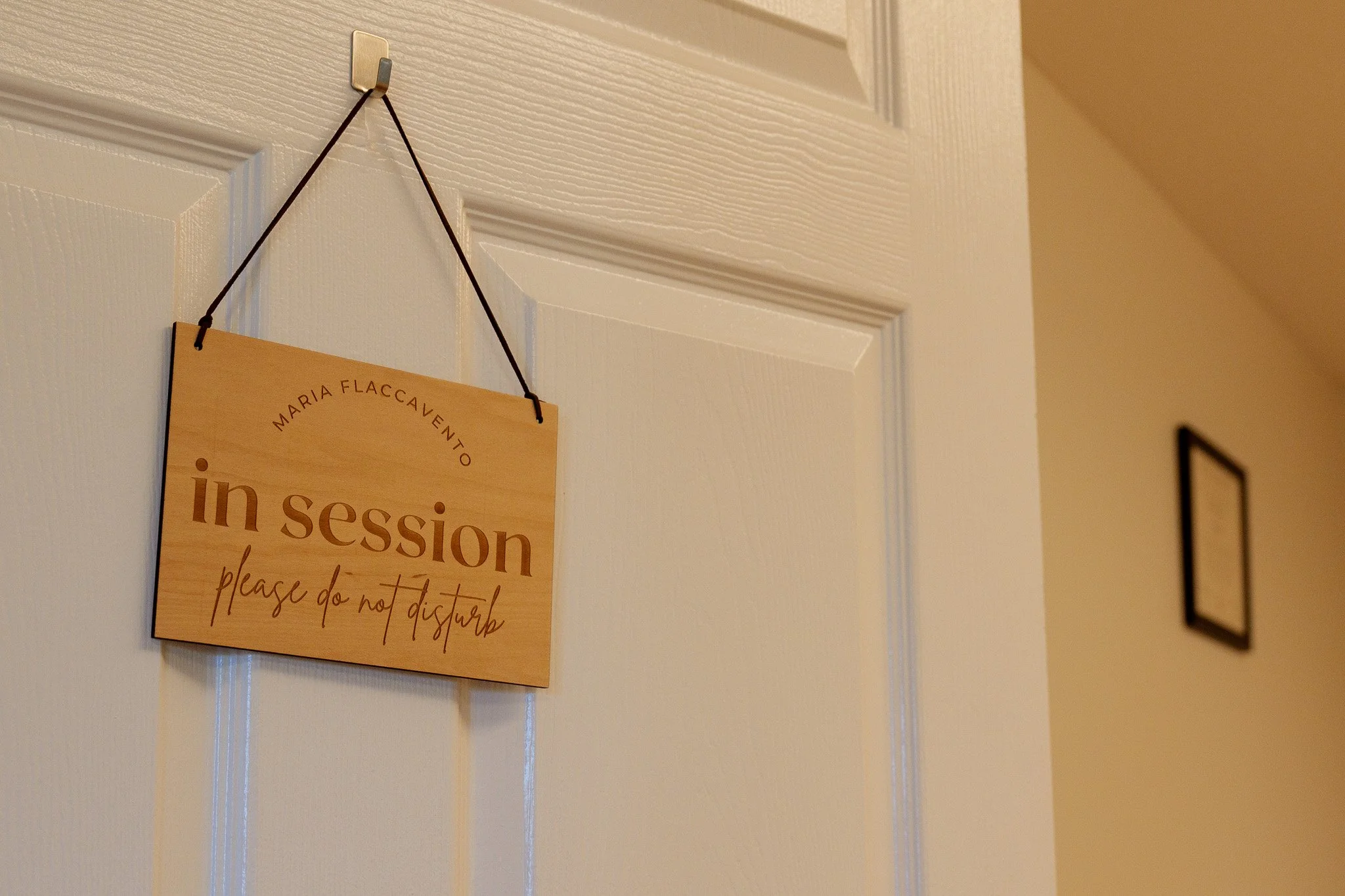 Wooden sign hanging on a door that says 'in session please do not disturb' with the name 'Maria Flaccaventto' at the top.