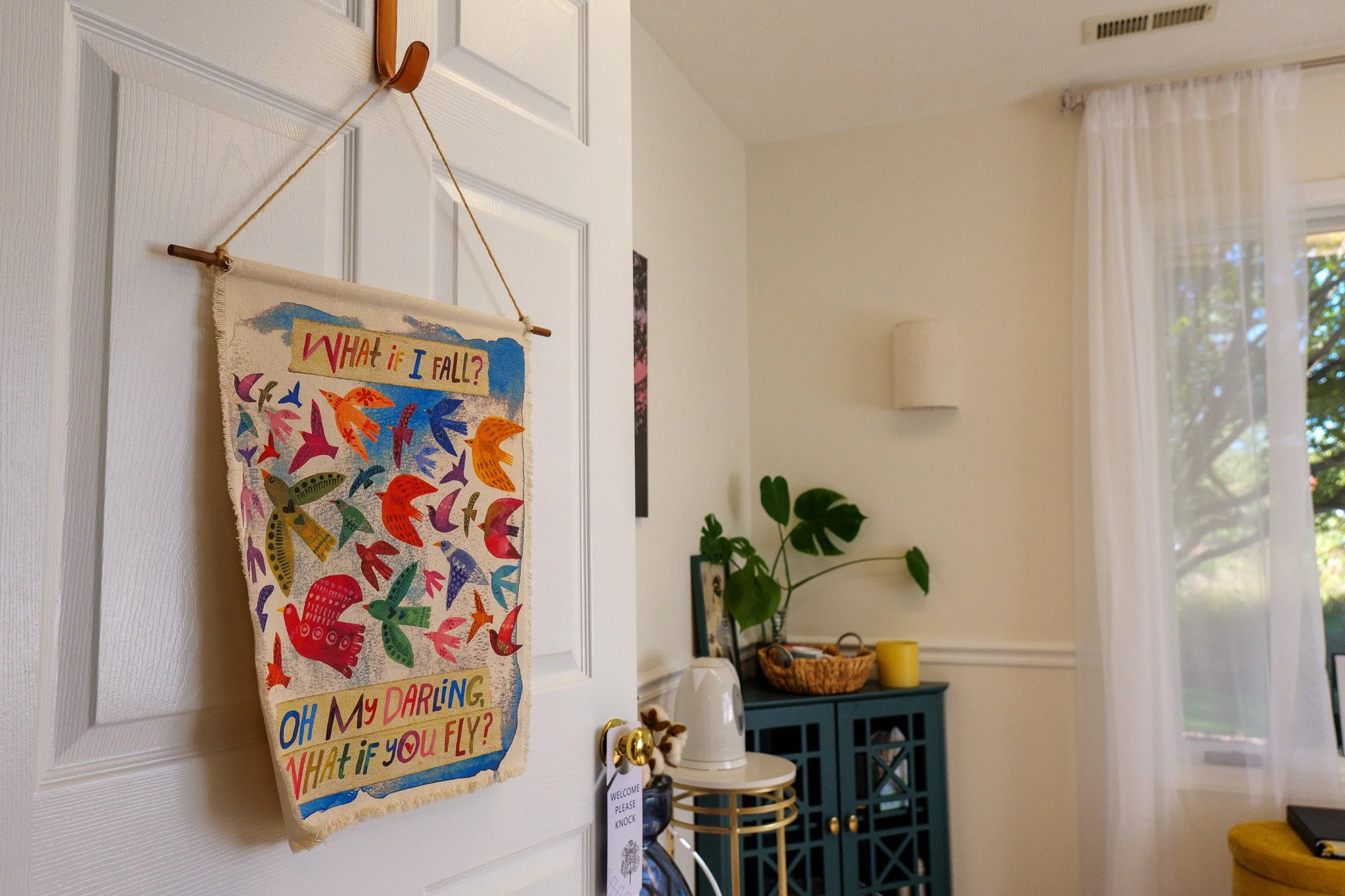 Decorative wall hanging with a colorful bird and flying design and the text 'What if I fall? Oh my darling, what if you fly?' on a white door.