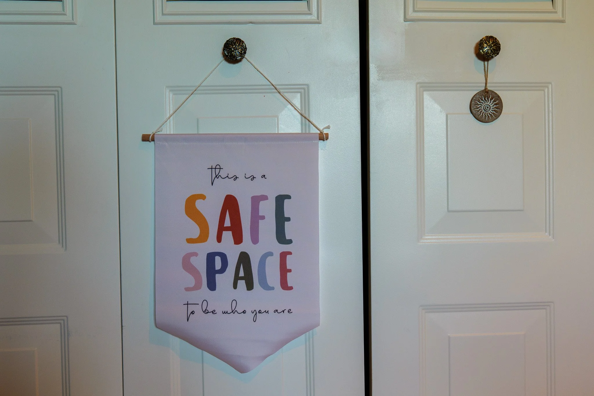 White closet doors with a decorative hanging sign that reads 'this is a SAFE SPACE to be who you are'