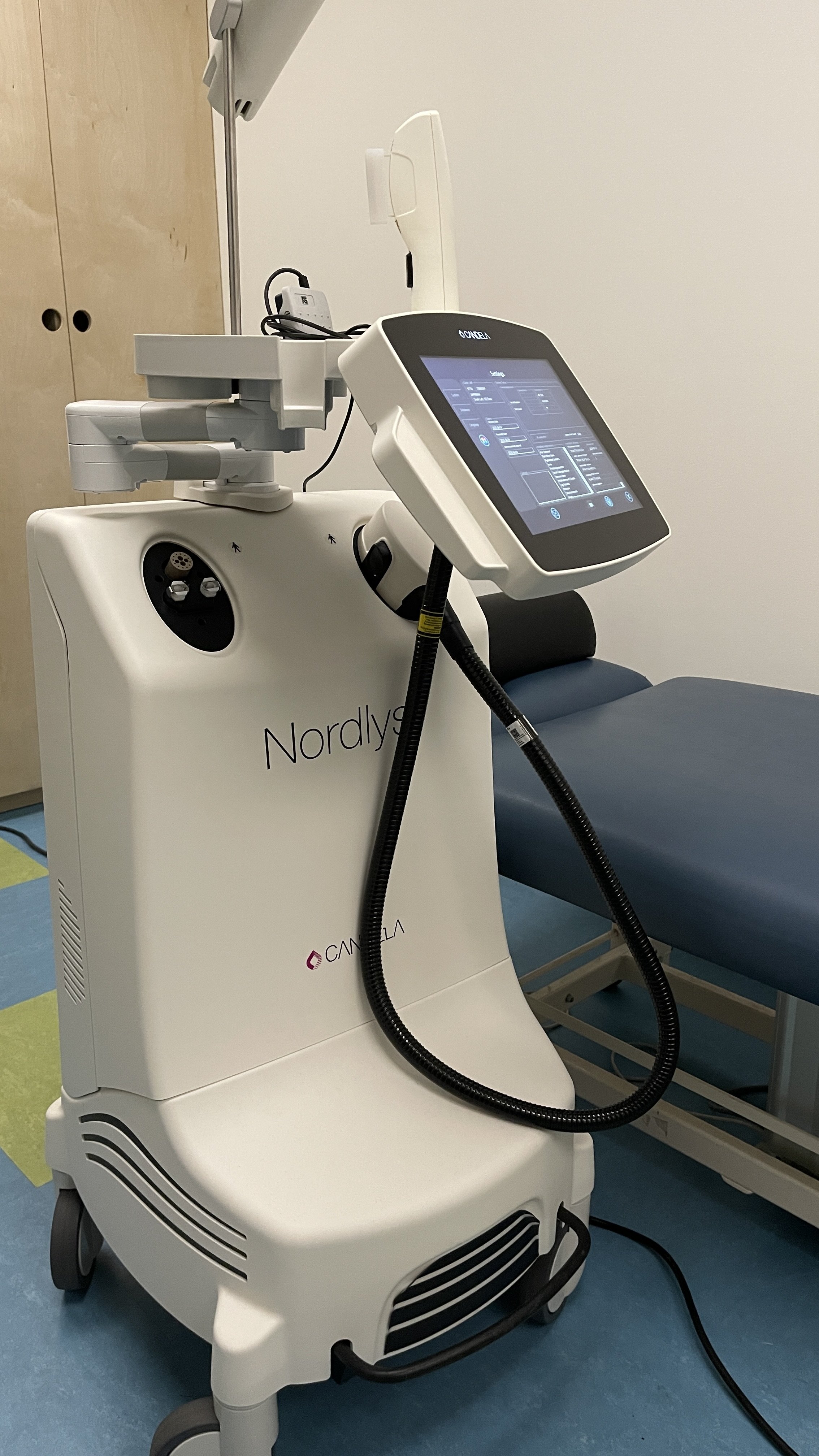 Medical device with a touchscreen monitor, labeled Nordlys, situated next to an examination table in a clinic room.