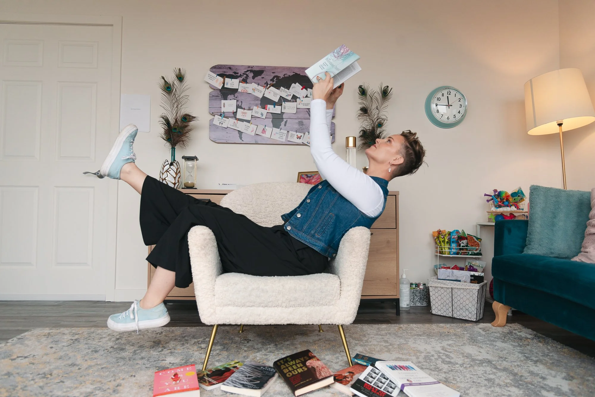 Brand photo of Edmonton psychologist, relaxing in a cozy living room, sitting on a cream-colored armchair with her legs up, reading a book.